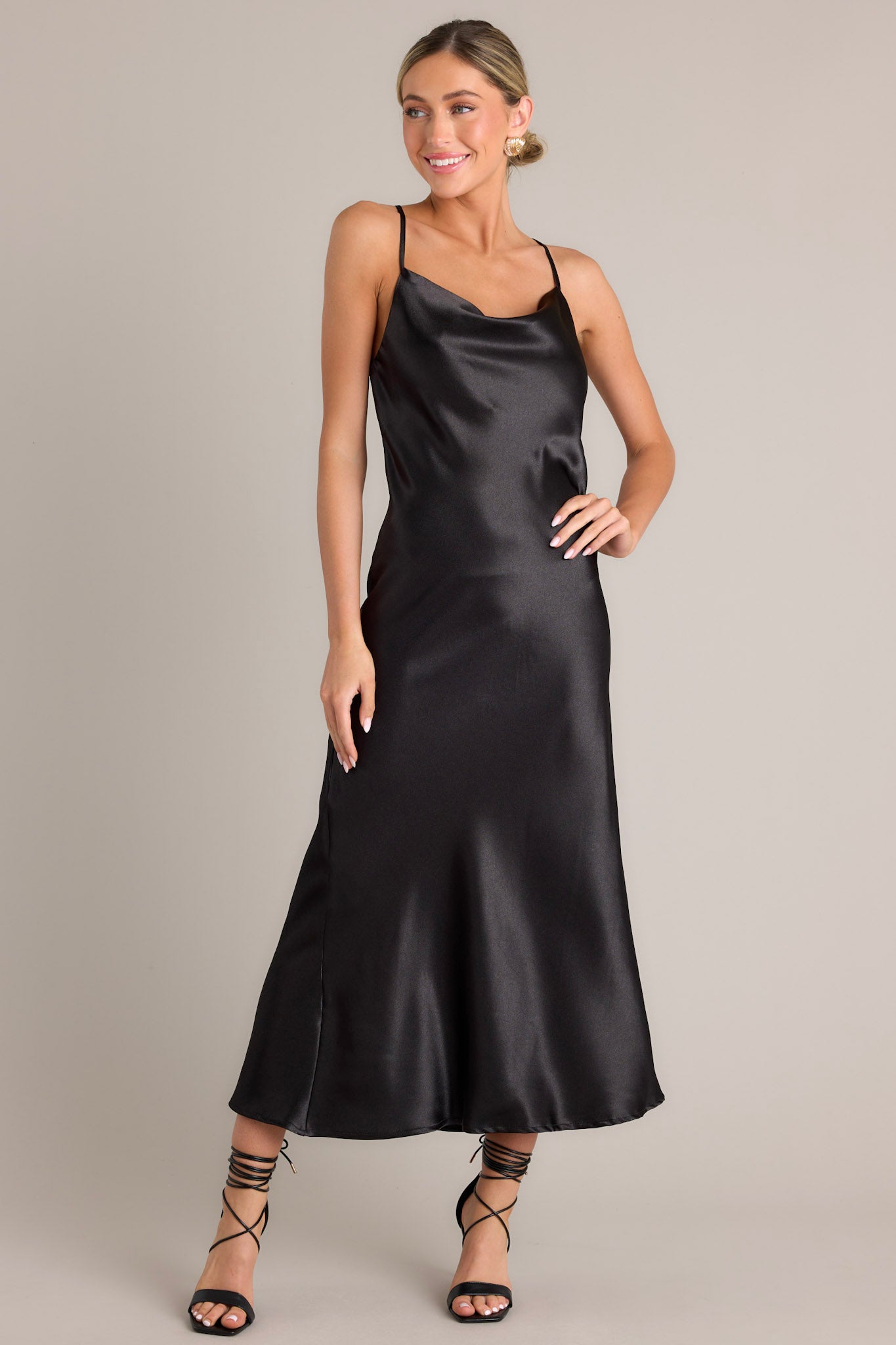 Full body view of this elegant black dress that features a satin-like fabric, adjustable straps, and a cowl neckline