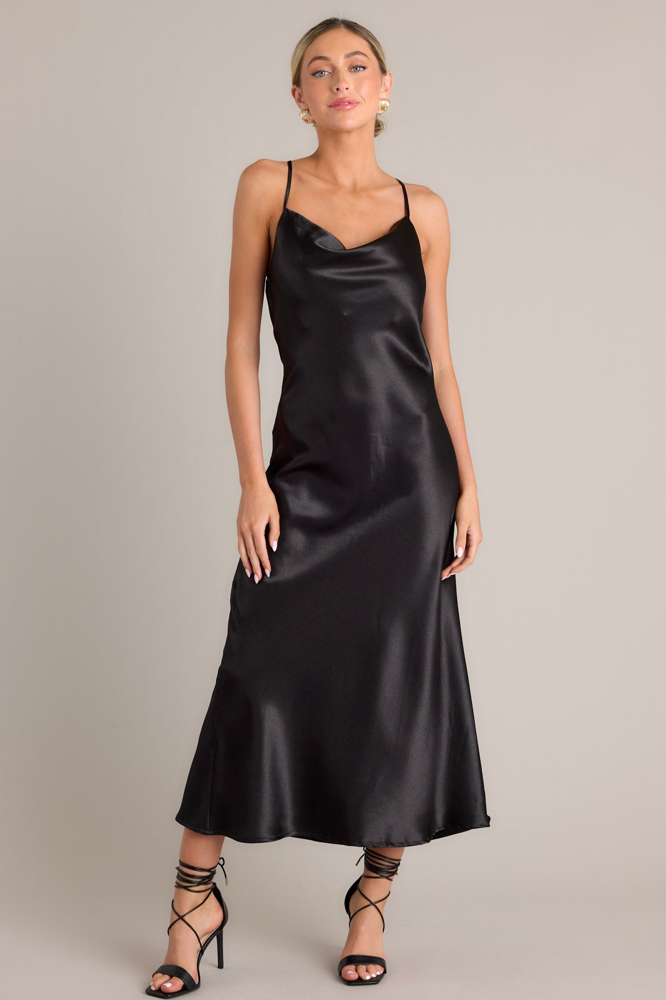 This elegant black dress features a satin-like fabric, adjustable straps, and a cowl neckline