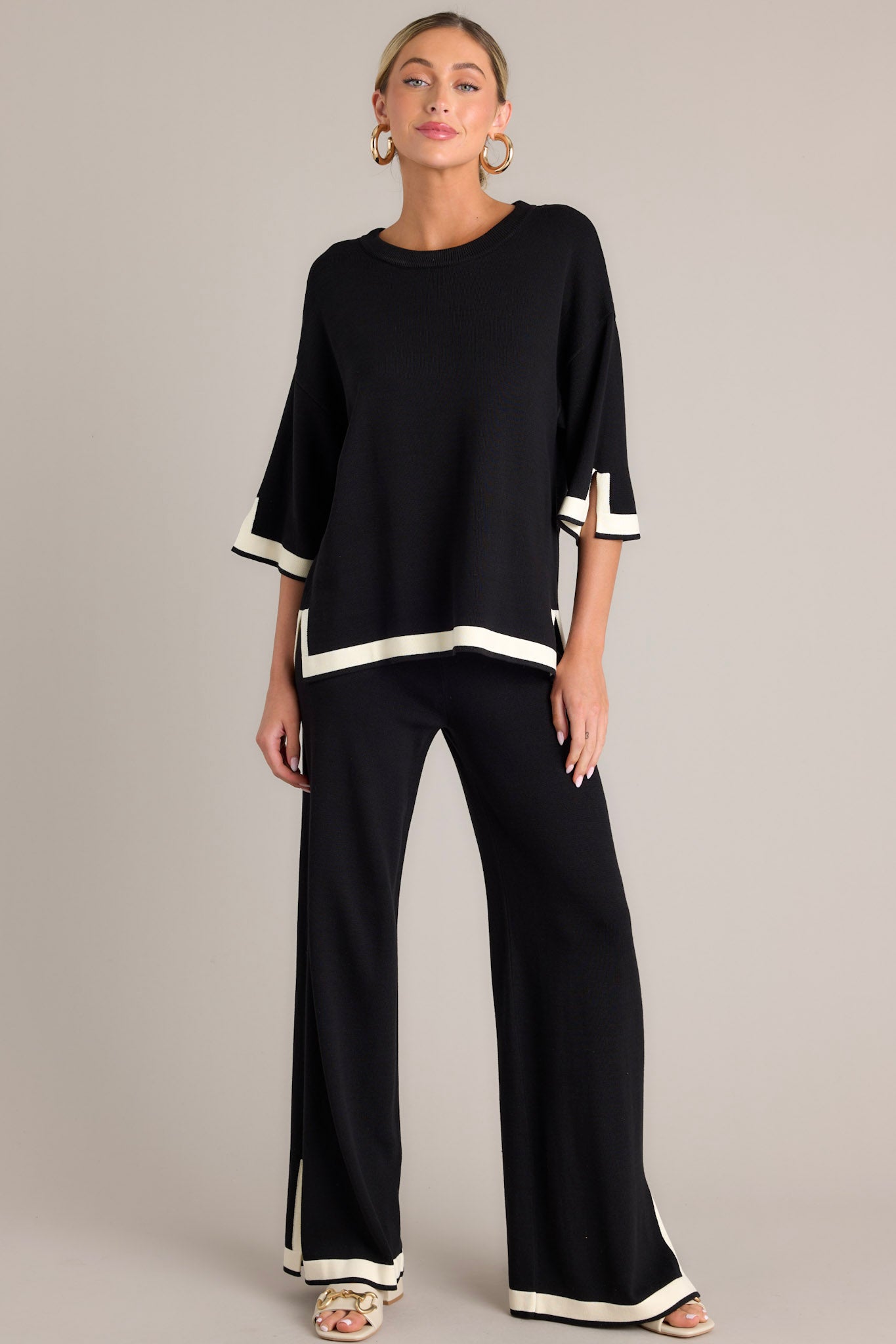 Full body view of these black sweater pants that feature a high waisted design, an elastic waistband, a wide leg, and a contrasting split hemline.