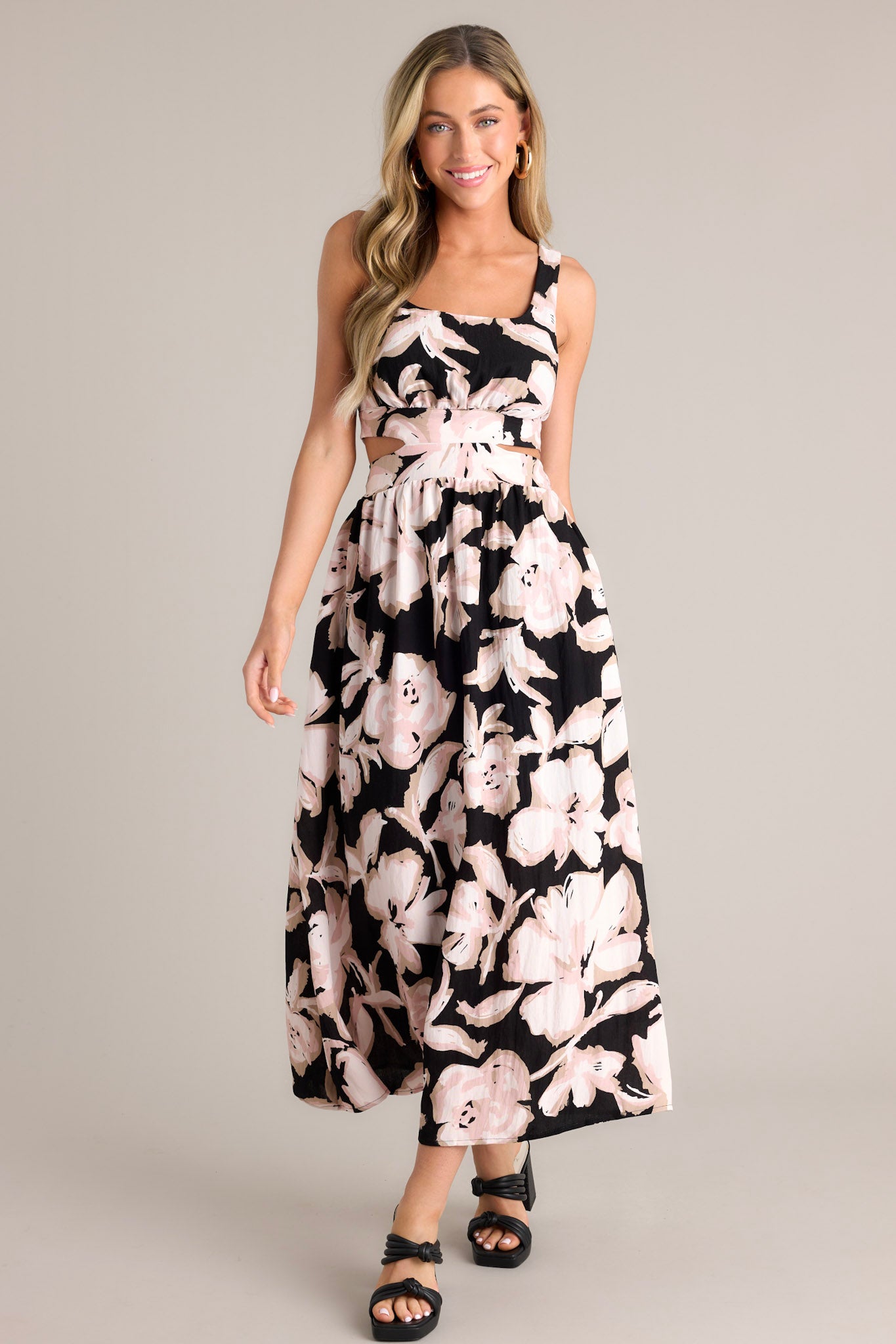 Front view of this black maxi dress that features a square neckline, thick straps, an elastic back insert, a self-tie back feature, waist cutouts with a smocked back insert, functional hip pockets, and an all over floral pattern.