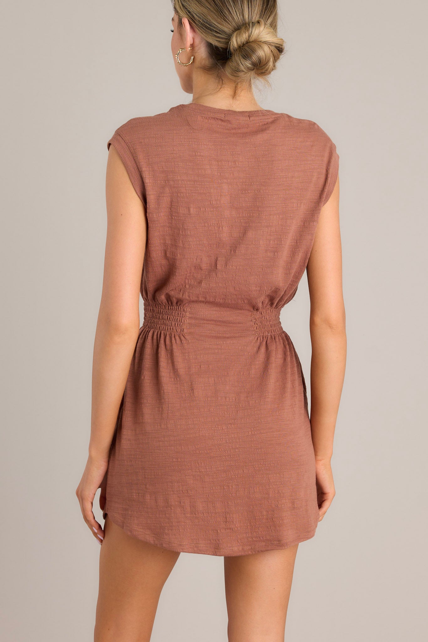 A back view of this dress that features a round neckline, smocked sections on either side of the waist, and a round hemline.