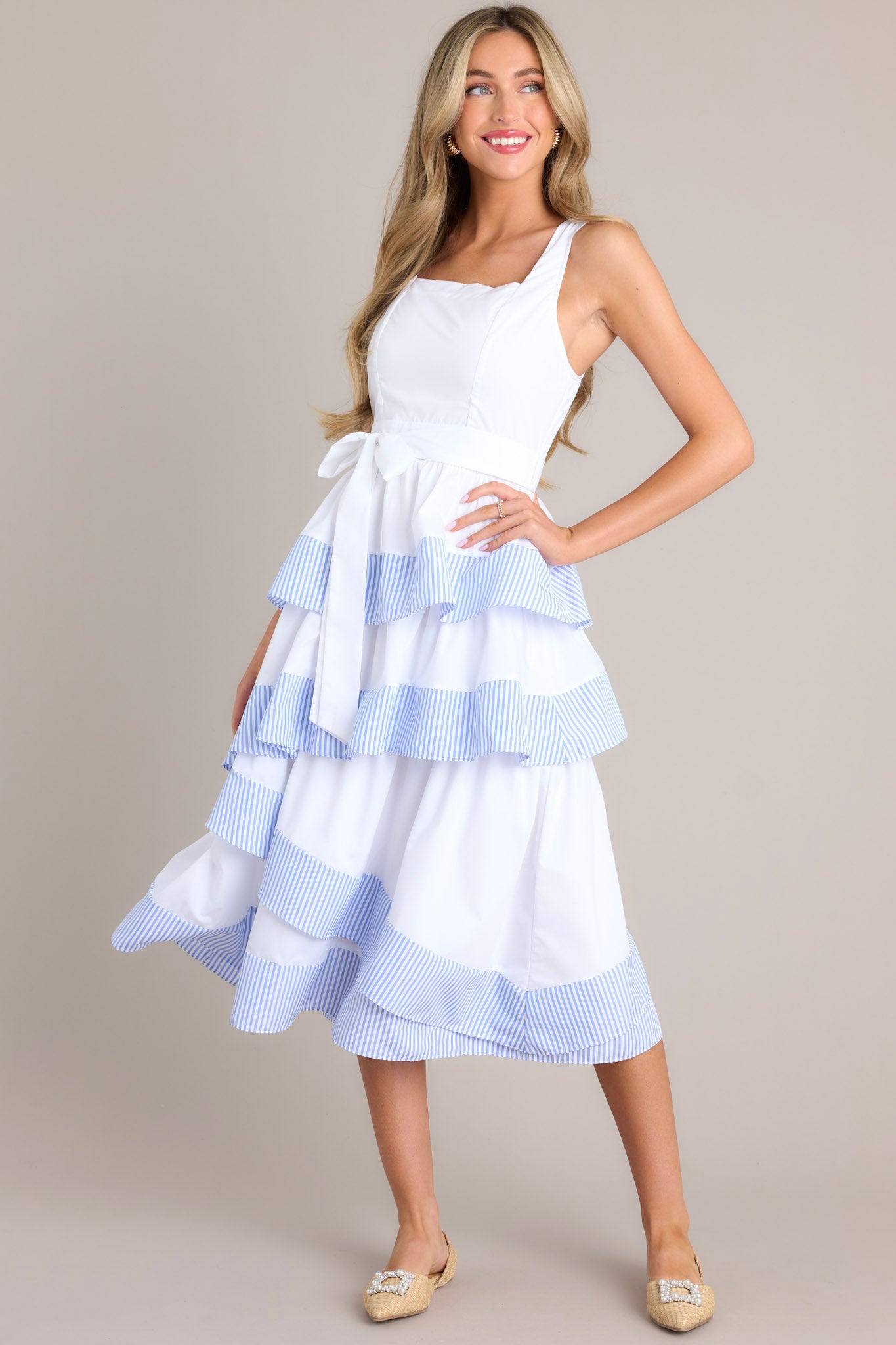 Full body view of this dress that features a square neckline, thick straps, a smocked back insert, a discrete zipper, a self-tie belt, belt loops, and an asymmetrical tiered design.