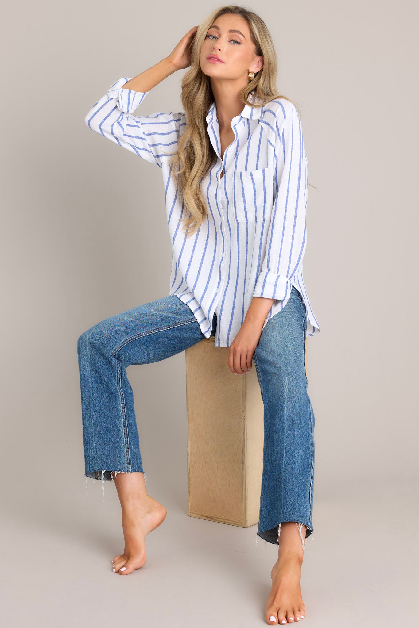 Sitting down view of this stripe top that features a collared neckline, a functional button front, a breast pocket, button cuffed long sleeves, and a split high low hemline.