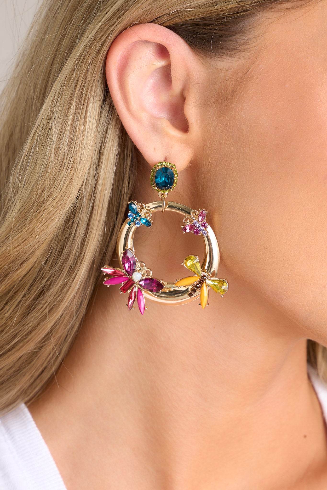 Close up view of these earrings that feature gold hardware, a rhinestone stud connected to a hoop design, colored butterfly shaped rhinestone details, and secure post backings.
