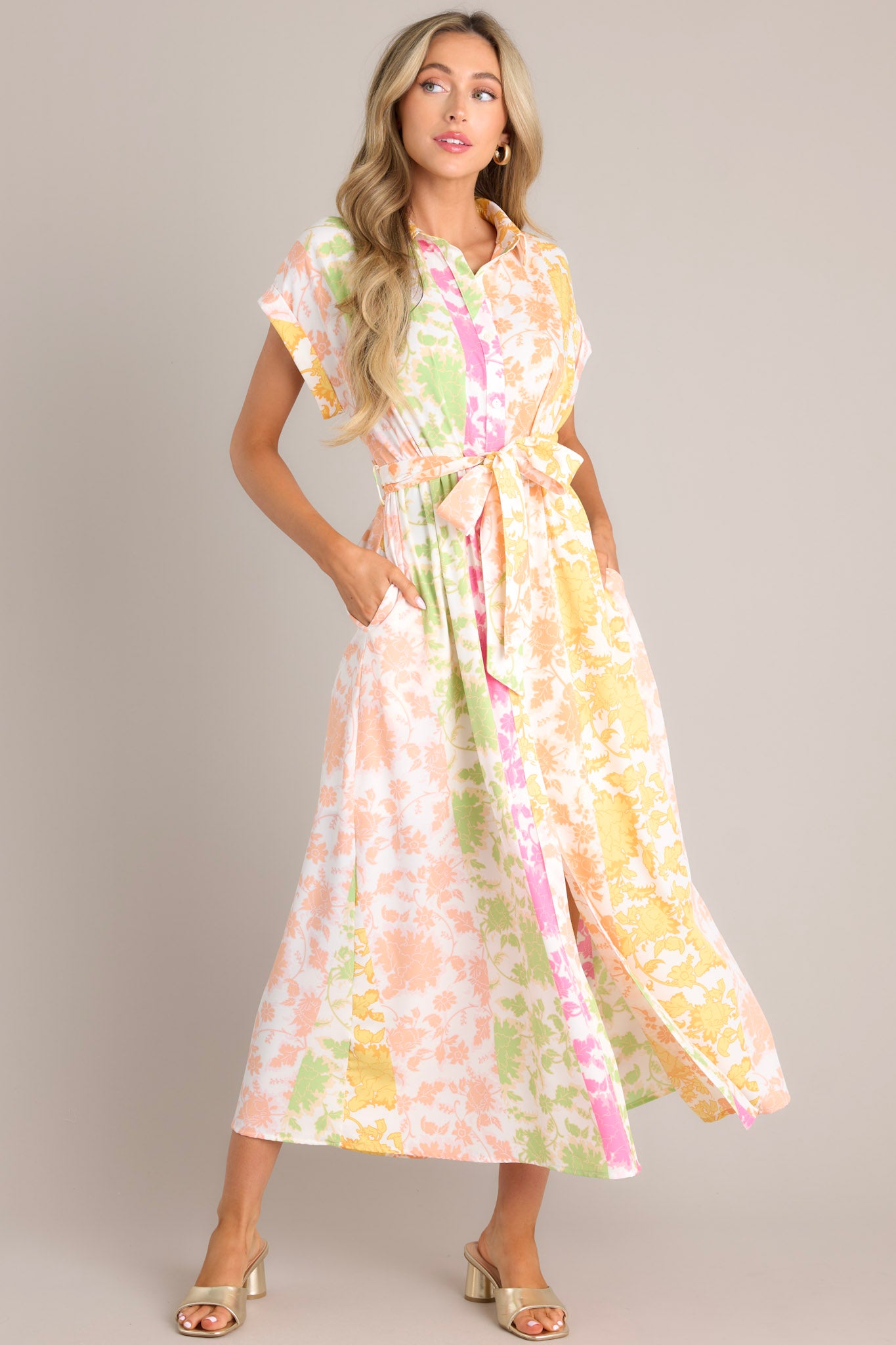 This multi floral dress features a collared neckline, a functional button front, gathering in the waist, a self-tie waist belt, belt loops, functional hip pockets, a front slit, and wide cuffed short sleeves.