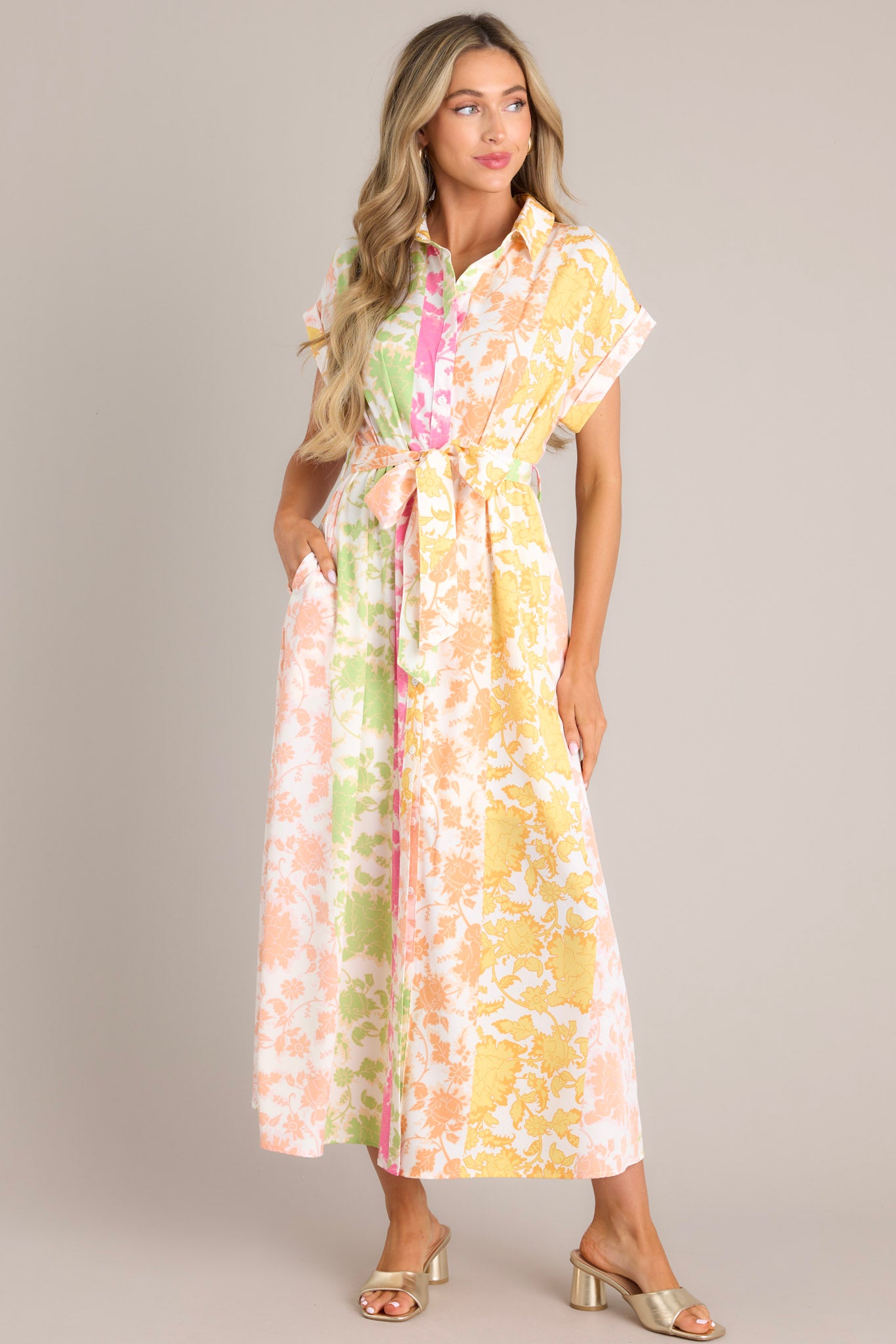 Full body view of this multi floral dress that features a collared neckline, a functional button front, gathering in the waist, a self-tie waist belt, belt loops, functional hip pockets, a front slit, and wide cuffed short sleeves.