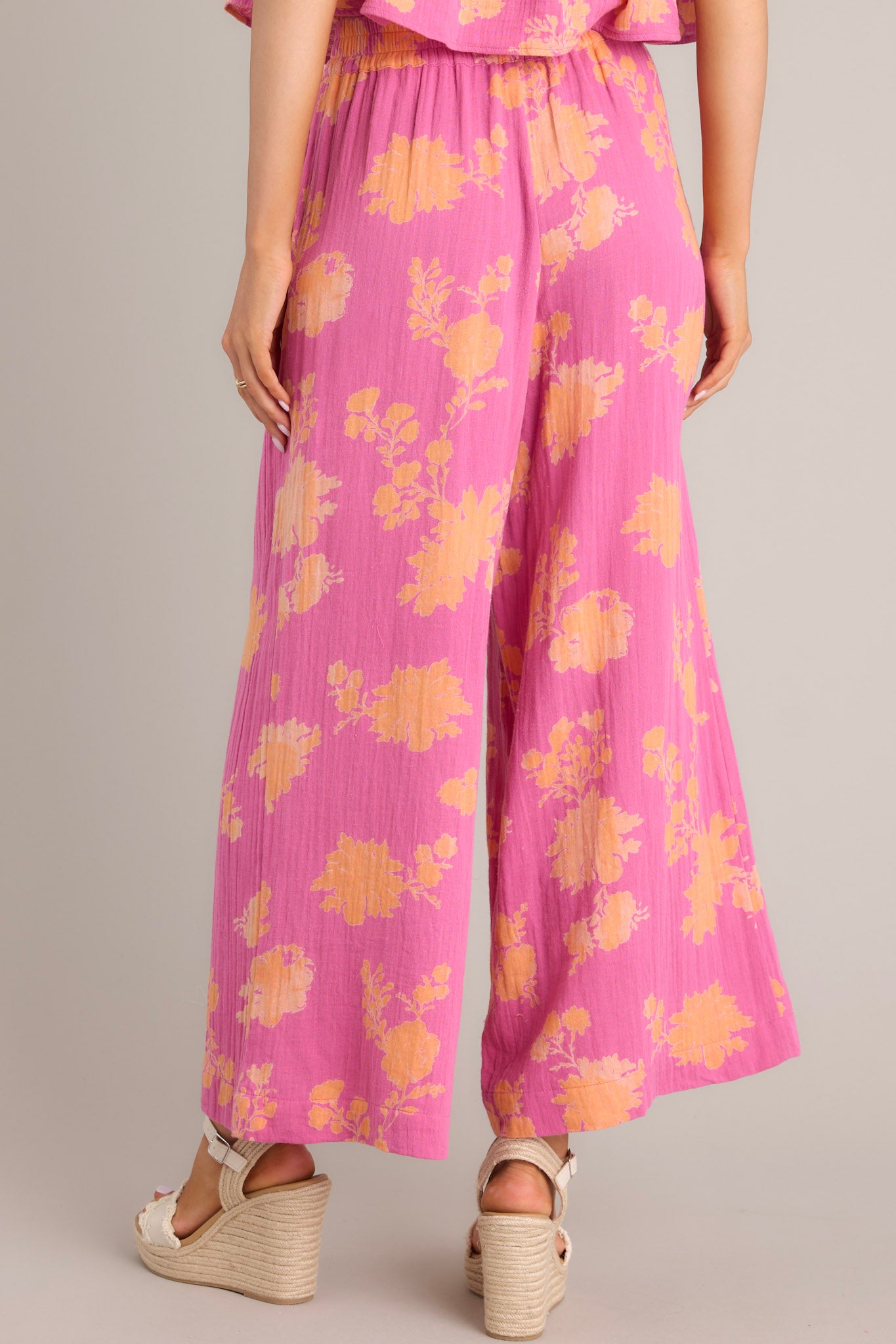 Back view of these pink floral pants that feature a high waisted design, a thick elastic waistband, functional hip pockets, and a wide leg.