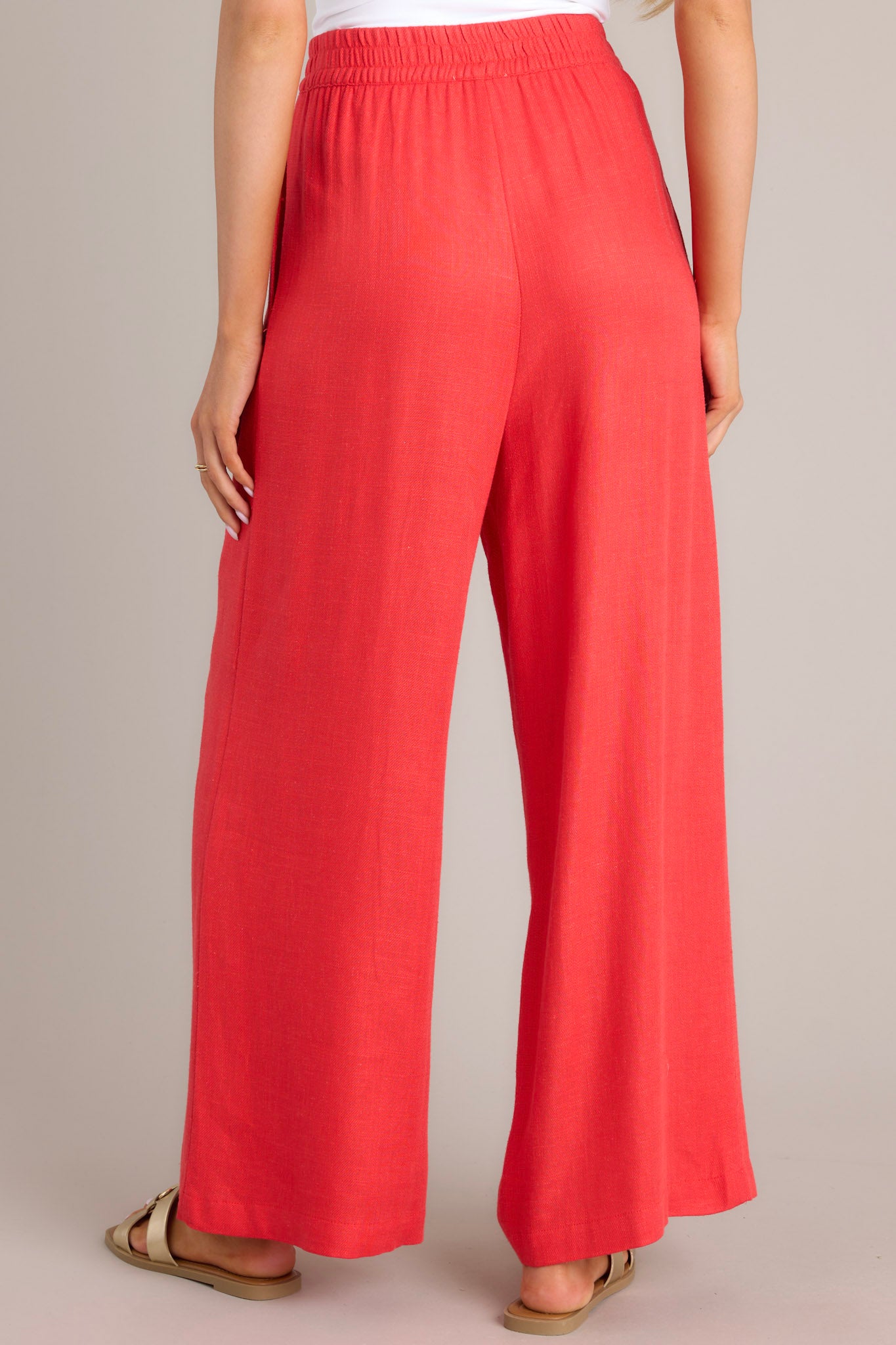 A back view of these pants that feature a high waisted design, an elastic insert in the back, functional hip pockets, a lightweight fabric, and a wide leg design.