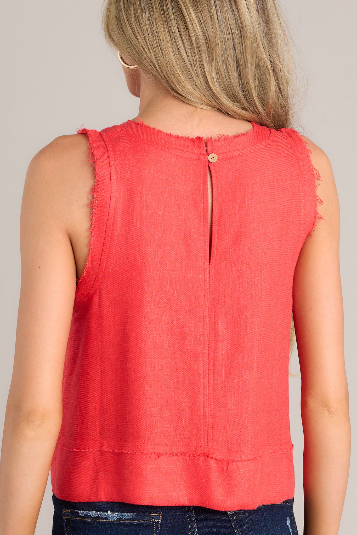 Back view of this tank that features a raw crew neckline, a keyhole with a button closure, a lightweight fabric, a split hemline, and a slightly cropped length.