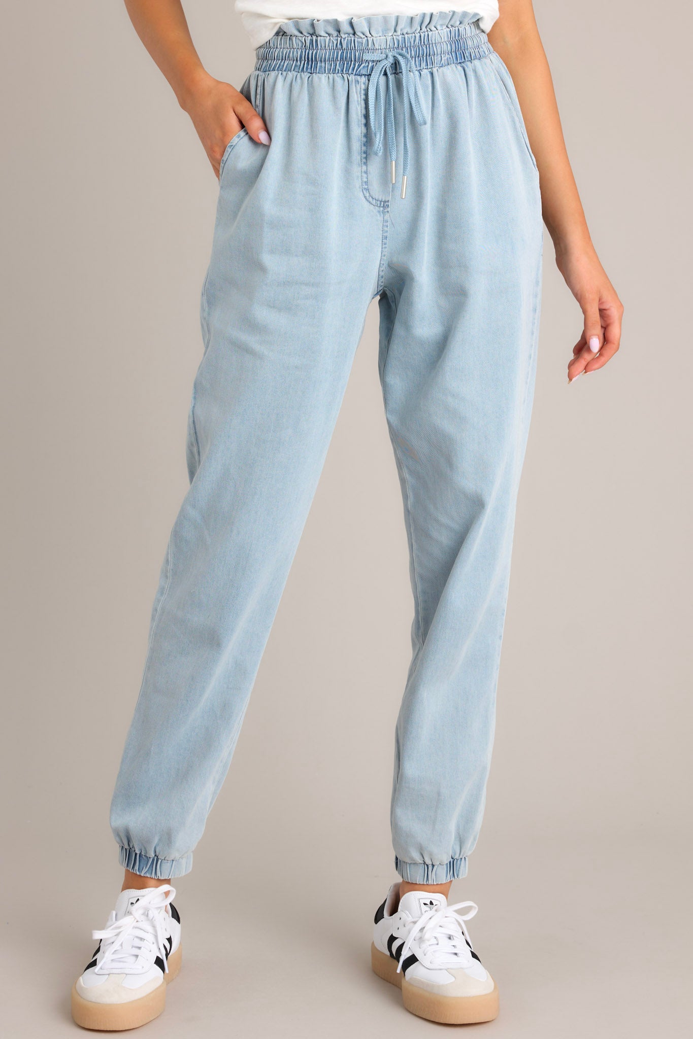 These light chambray joggers feature a high waisted design, an elastic paper bag waistband, a self-tie drawstring, functional hip & back pockets, and elastic cuffed ankles.