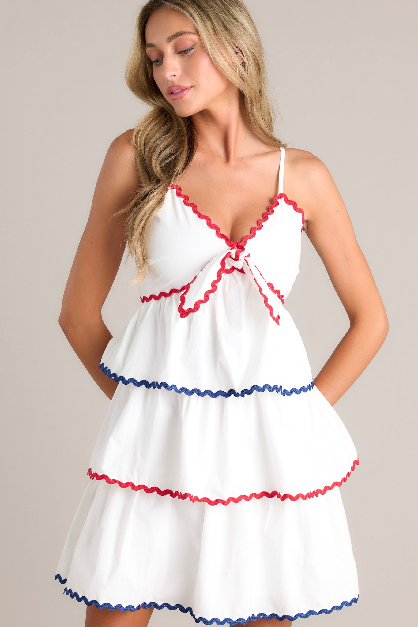 Front view of this dress that features a v-neckline, thin adjustable straps, a smocked back insert, a discrete back zipper, a self-tie bust feature, a tiered design, and ricrac hemlines.