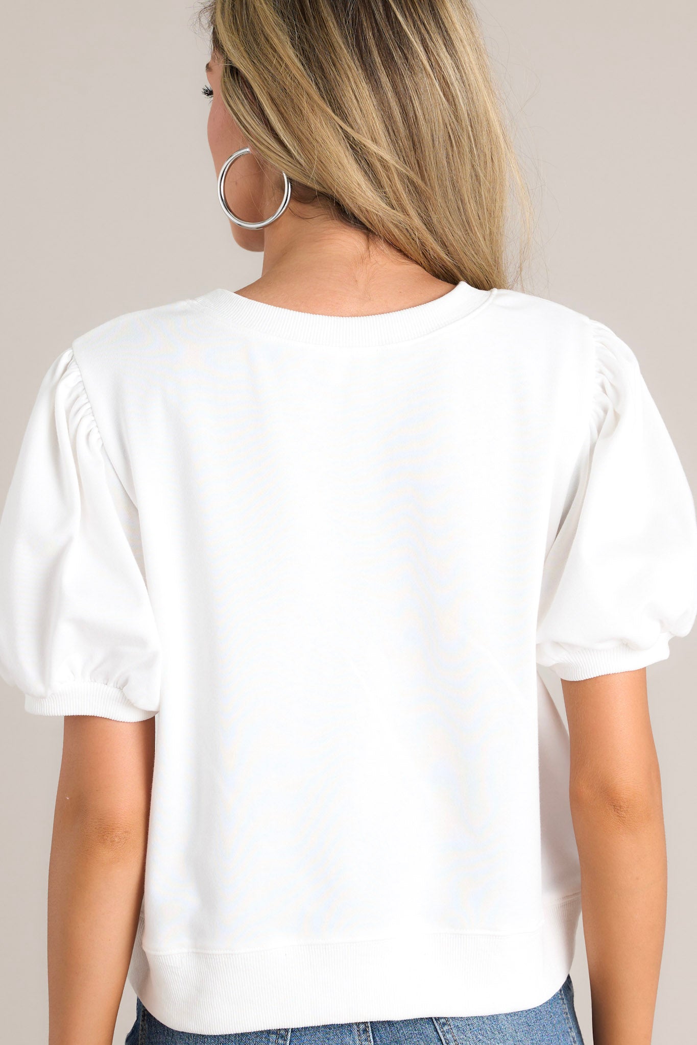 Back view of this white top that features a crew neckline, festive sequin detailing, ribbed cuffed puff sleeves, and a ribbed hemline.