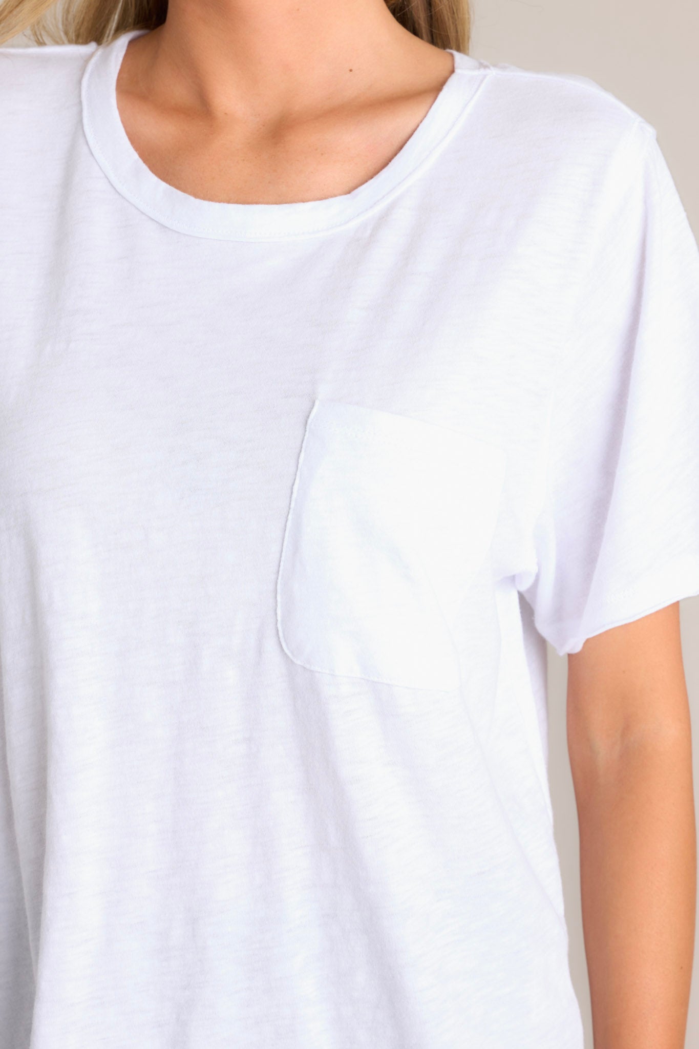 Close up view of this white tee that features a crew neckline, a functional breast pocket, a raw hemline, and short sleeves.