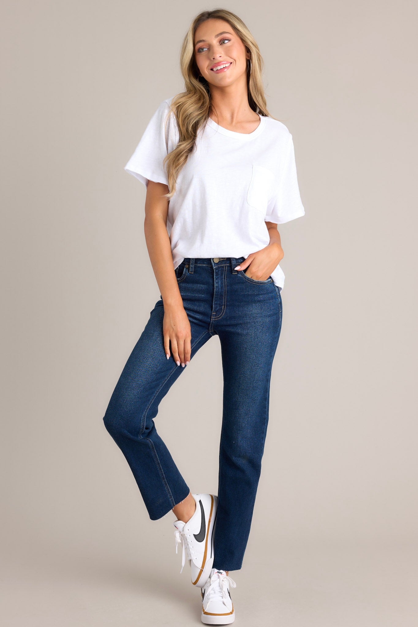 Full length view of dark wash denim jeans with a high-rise waist, scissor cut-off hem, functional pockets, belt loops, and a zipper button closure