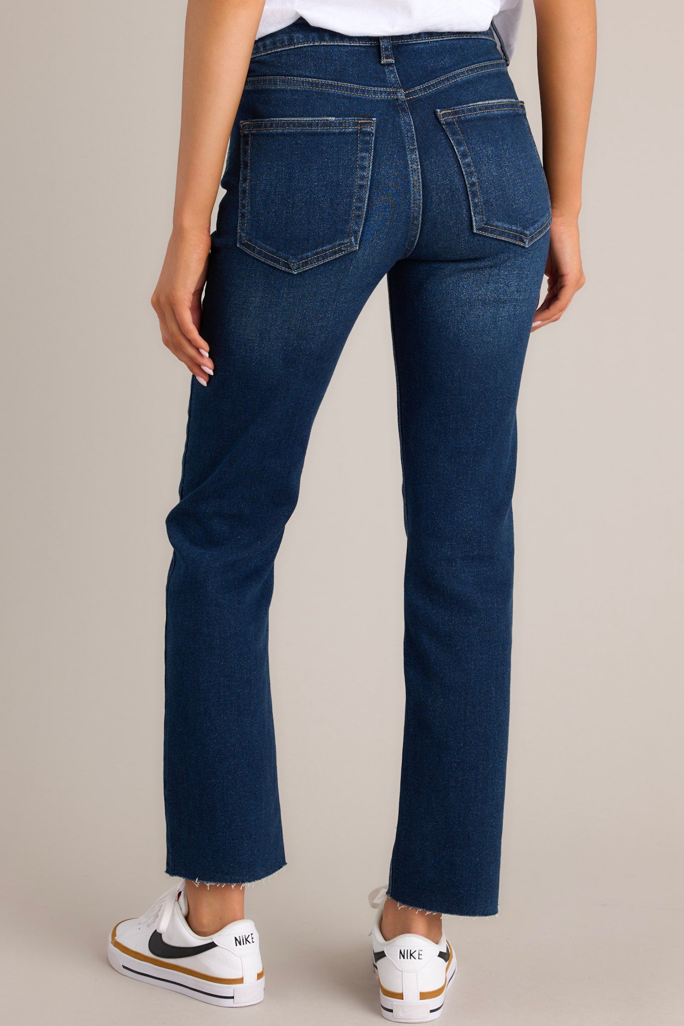 Back view of dark wash denim jeans highlighting the high-rise waist, functional back pockets, belt loops, and scissor cut-off hem.