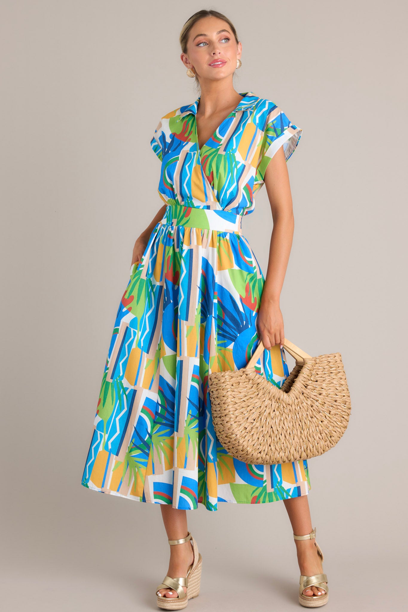 Front angled view of a colorful wrap dress with an abstract blue, green, yellow, and red pattern, featuring a cinched waist and cap sleeves