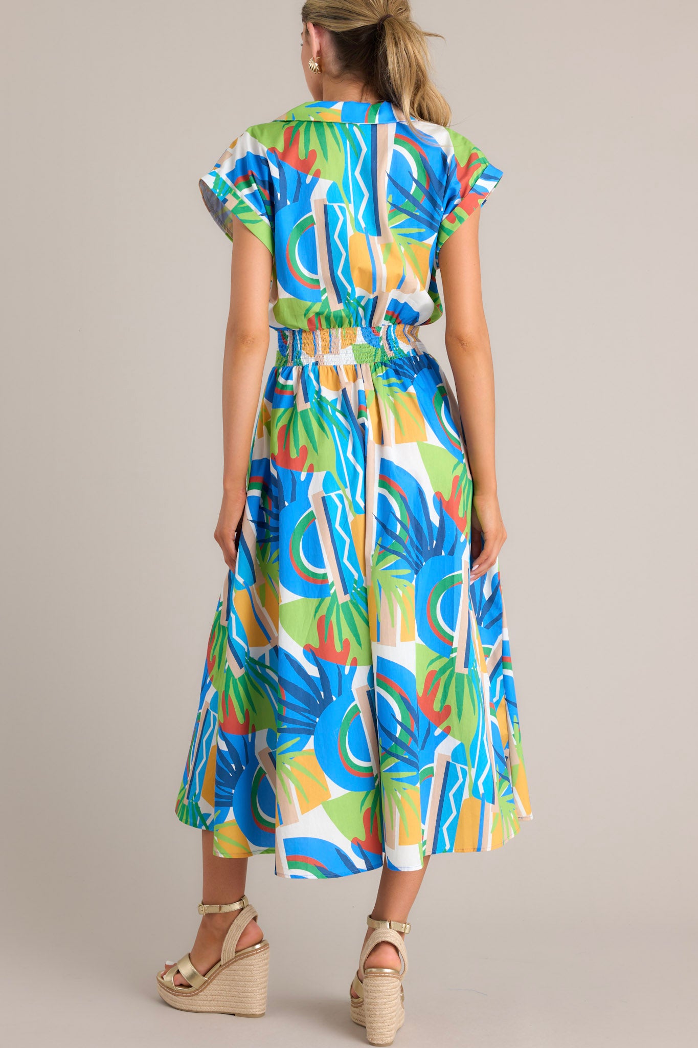 Back view of a colorful wrap dress with an abstract blue, green, yellow, and red pattern, highlighting the cinched waist and cap sleeves.