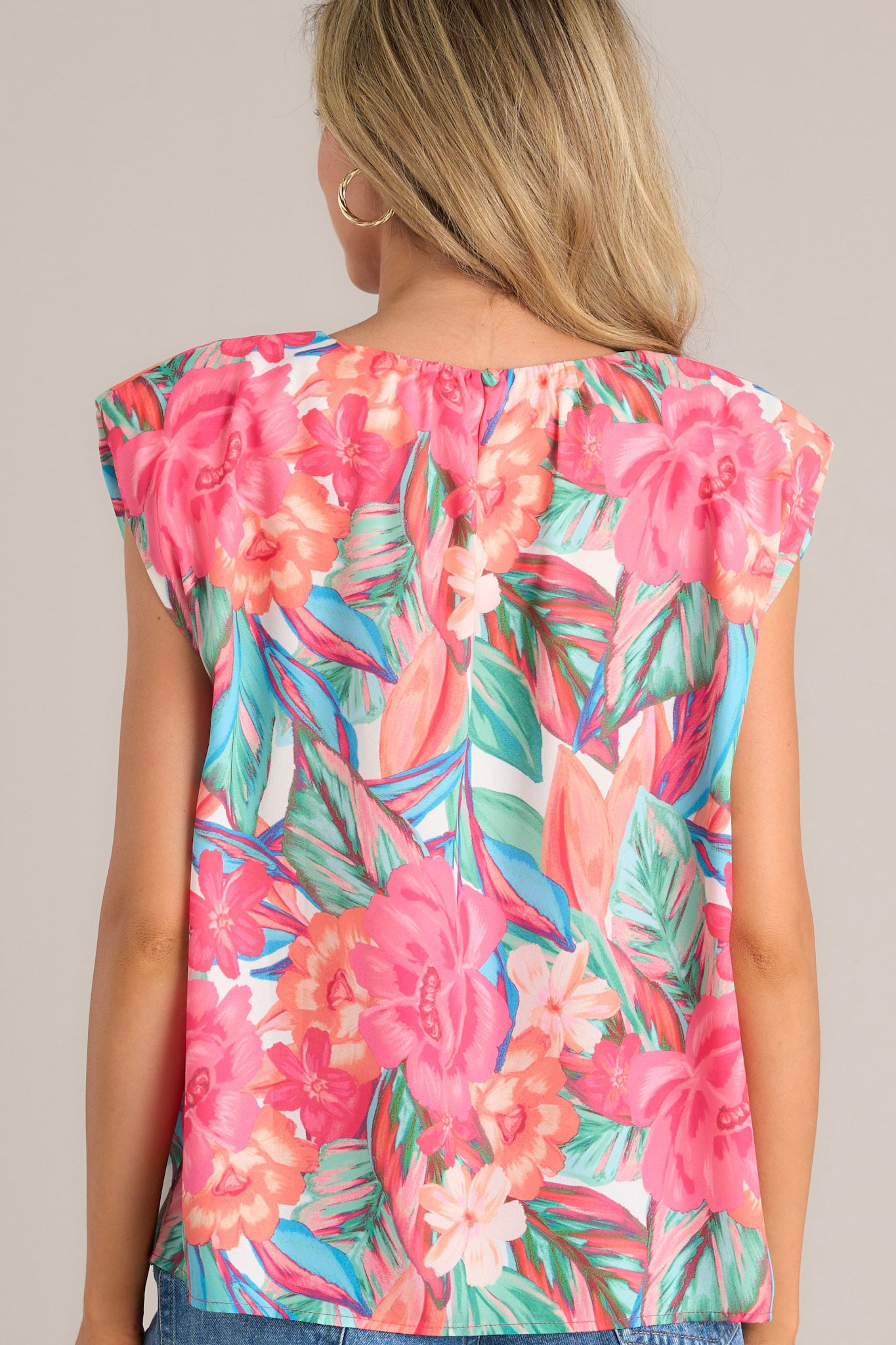 Back view of this hot pink floral top that features a crew neckline, shoulder padding, wide short sleeves, and a tropical floral print.