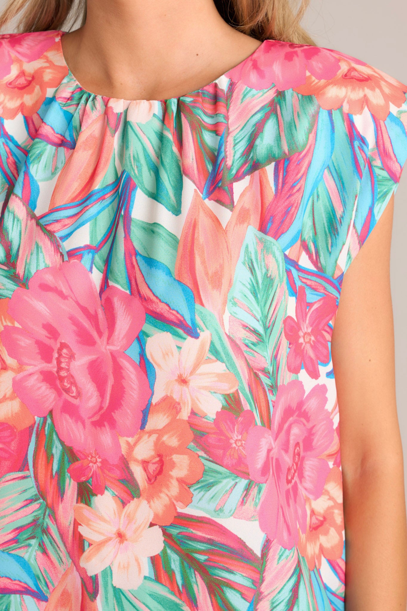 Close up view of this hot pink floral top that features a crew neckline, shoulder padding, wide short sleeves, and a tropical floral print.