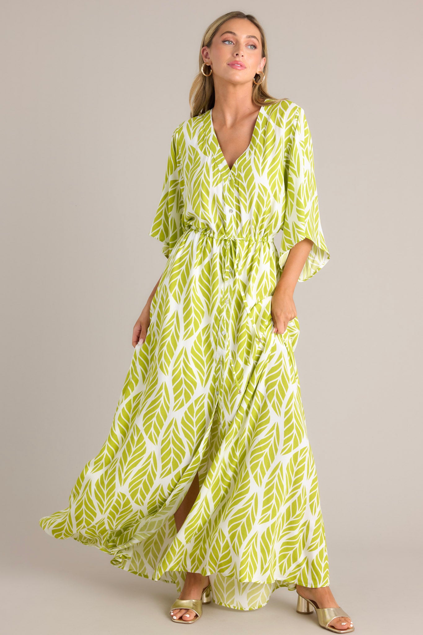 Angled full body view of this lime green maxi dress that features a v-neckline, a functional button front, a self-tie drawstring waist, a flowing silhouette, and flowing half sleeves.