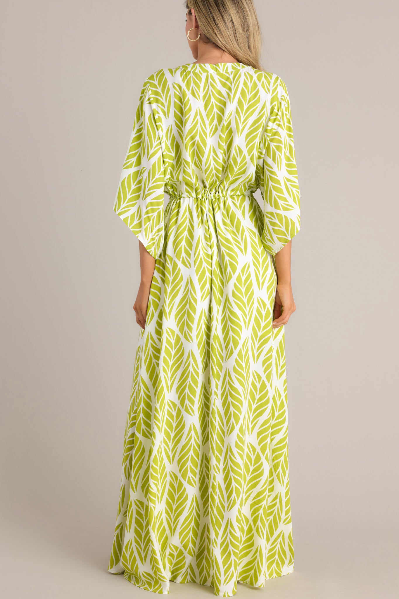 Back view of this lime green maxi dress that features a v-neckline, a functional button front, a self-tie drawstring waist, a flowing silhouette, and flowing half sleeves.