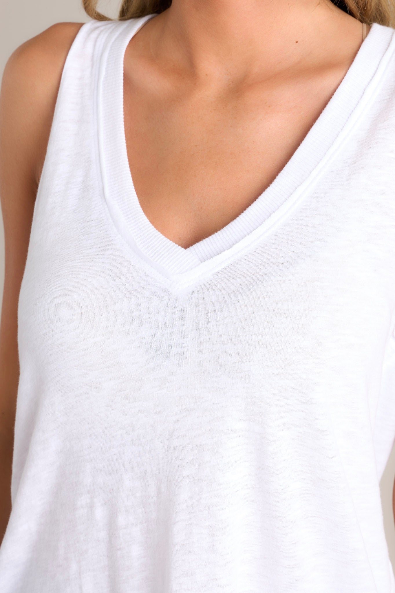 Close up view of this white tank that features a v-neckline, a sleeveless design, a classic color, and a scoop hemline.