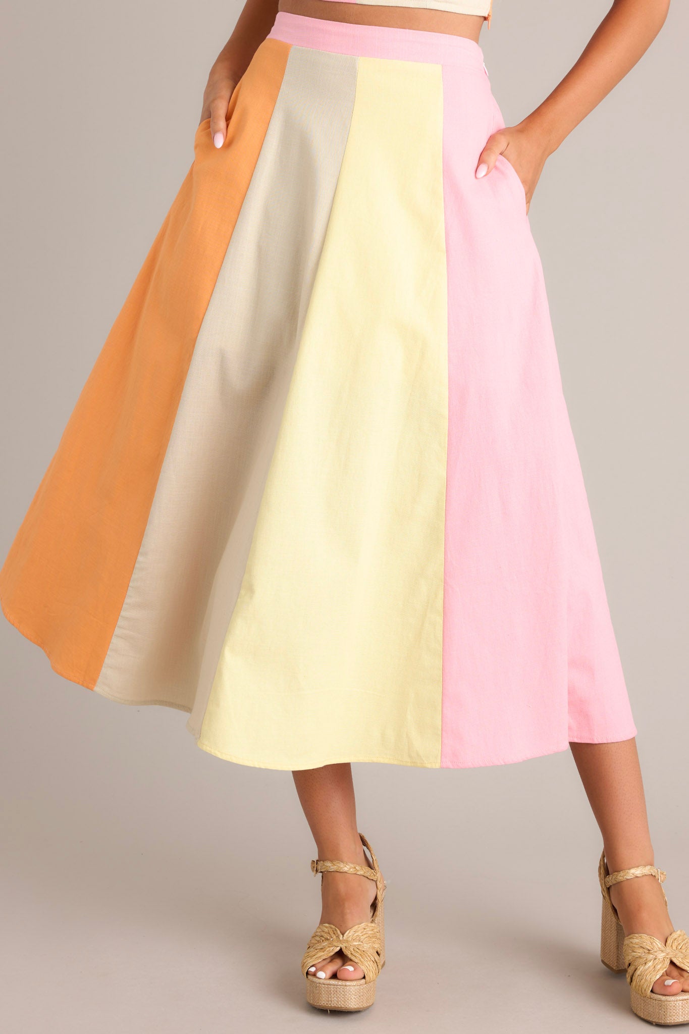 Front view of this pastel midi skirt that features a high waisted design, an elastic insert in the back of the waist, a discrete side zipper, functional hip pockets, and a flowing silhouette.