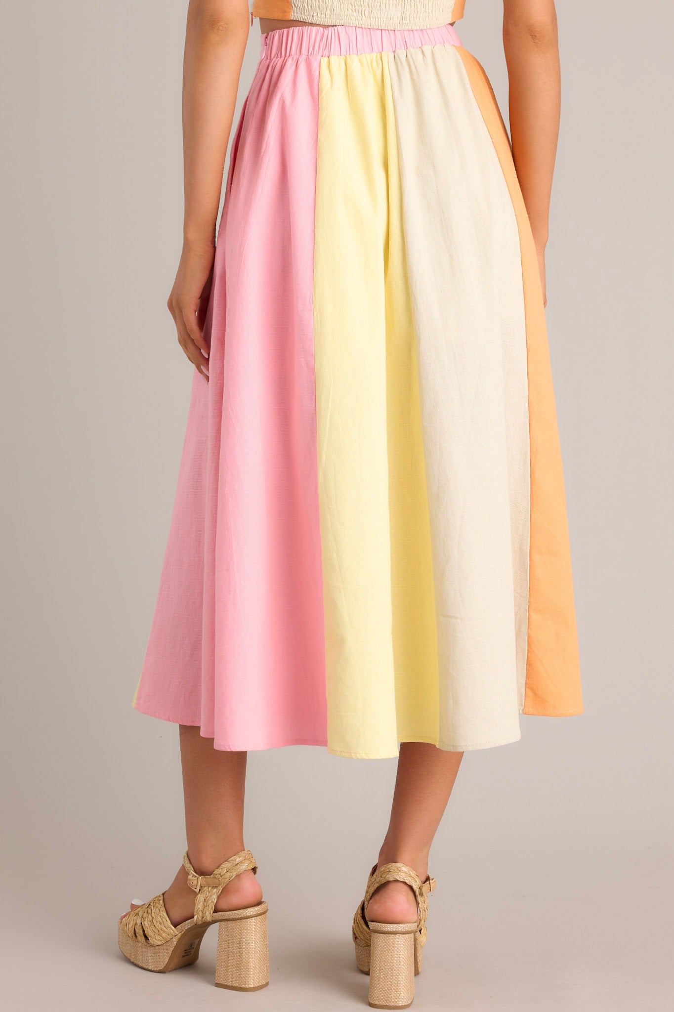 Back view of this pastel midi skirt that features a high waisted design, an elastic insert in the back of the waist, a discrete side zipper, functional hip pockets, and a flowing silhouette.