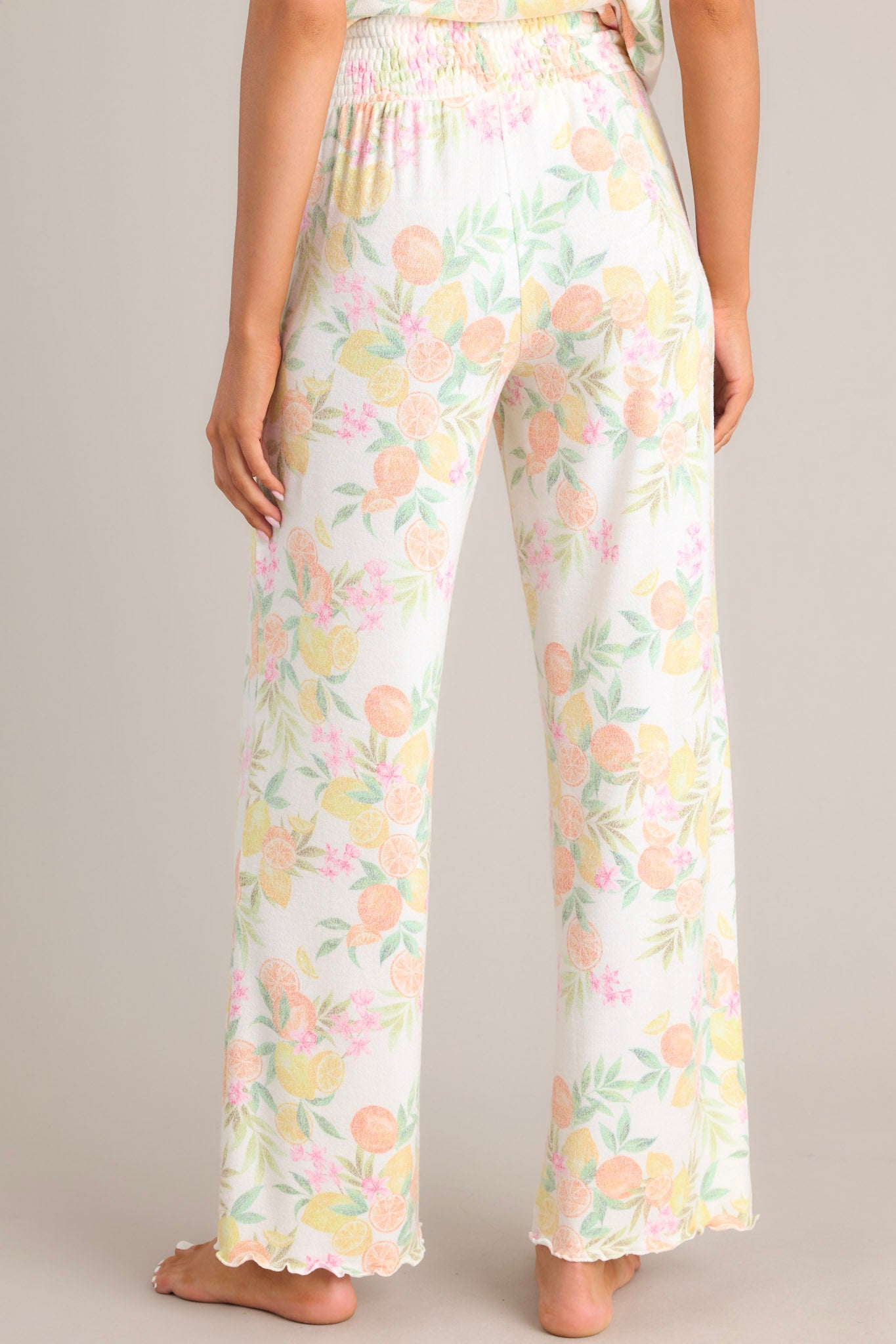 Back view of these white citrus pants that feature a high waisted design, a fully smocked waistband, a super soft material, a wide leg, and a scalloped hemline.