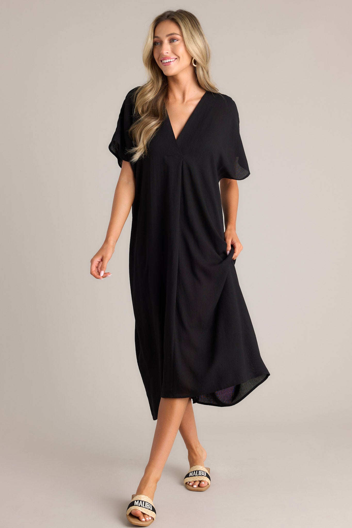 Side view of this black cover up that features a v-neckline, short dolman sleeves, and a comfortable oversized fit.