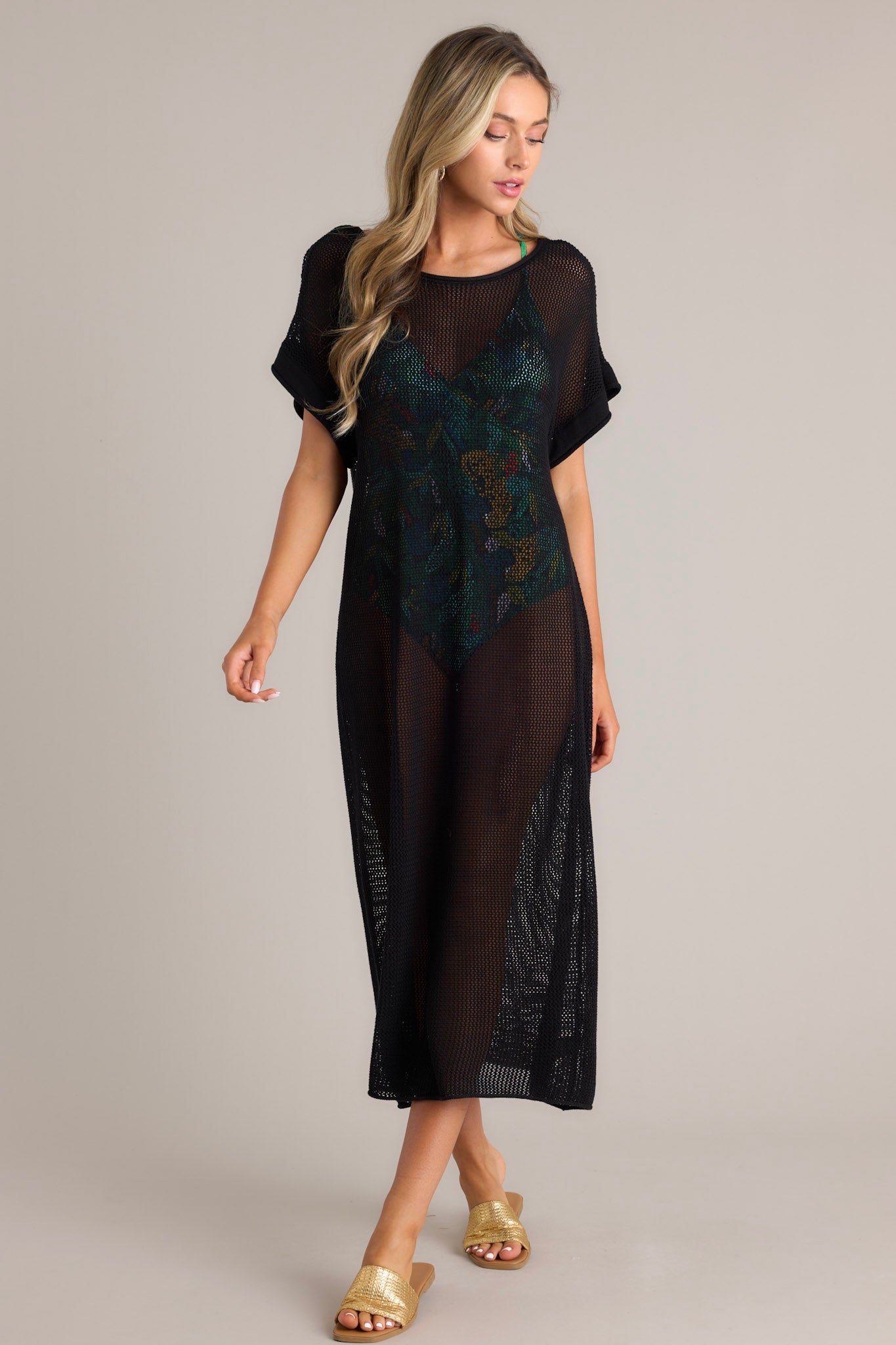 Angled full body view of this black cover-up dress that features a wide rounded neckline, open back feature, an open-knit design, and cuffed short sleeves.