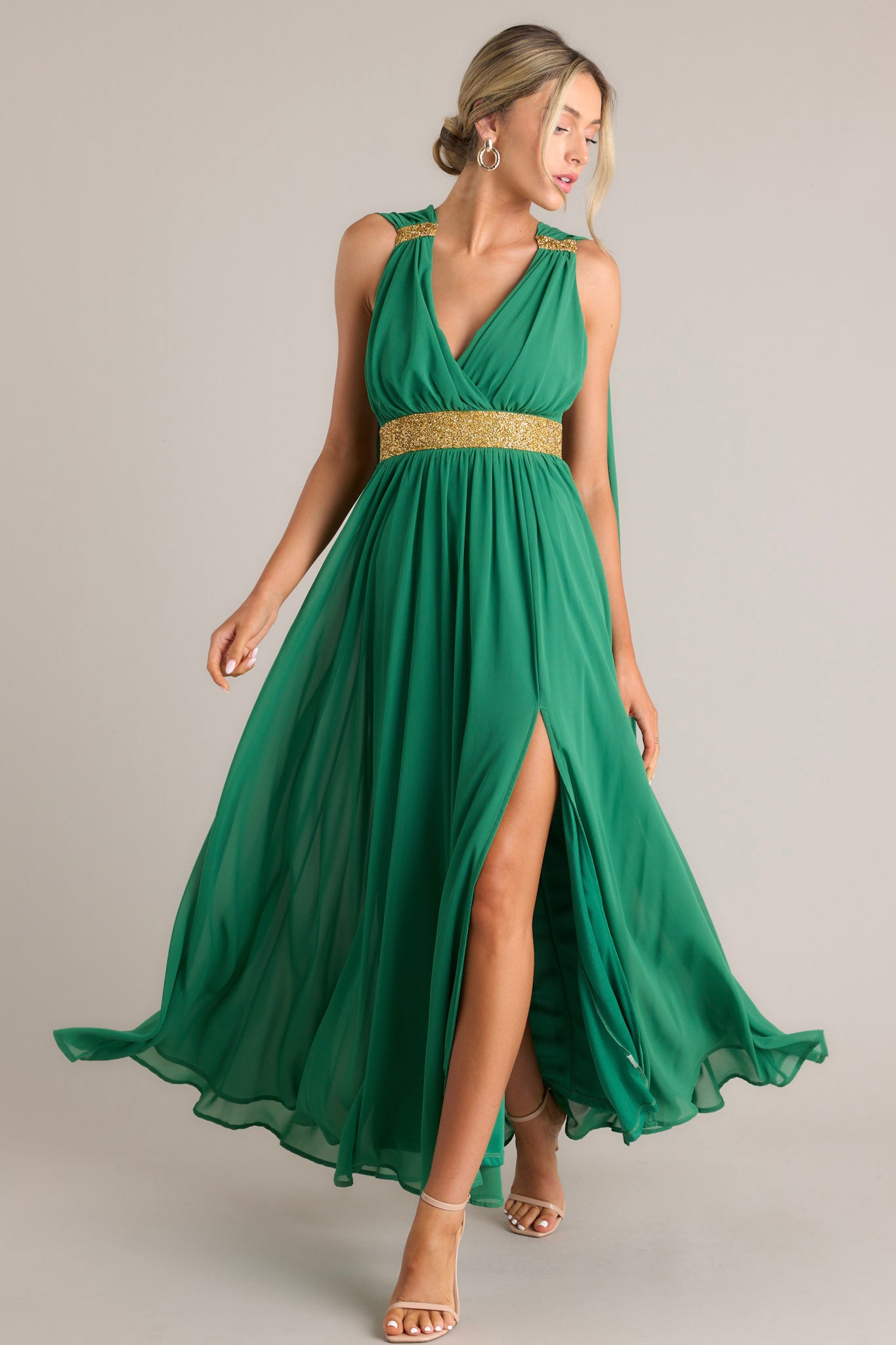 This green dress features a v-neckline, adjustable crisscross straps down the back, rhinestone detailing, fabric trailing from the shoulder to the bottom of the dress, and a slit on the left side of the skirt.