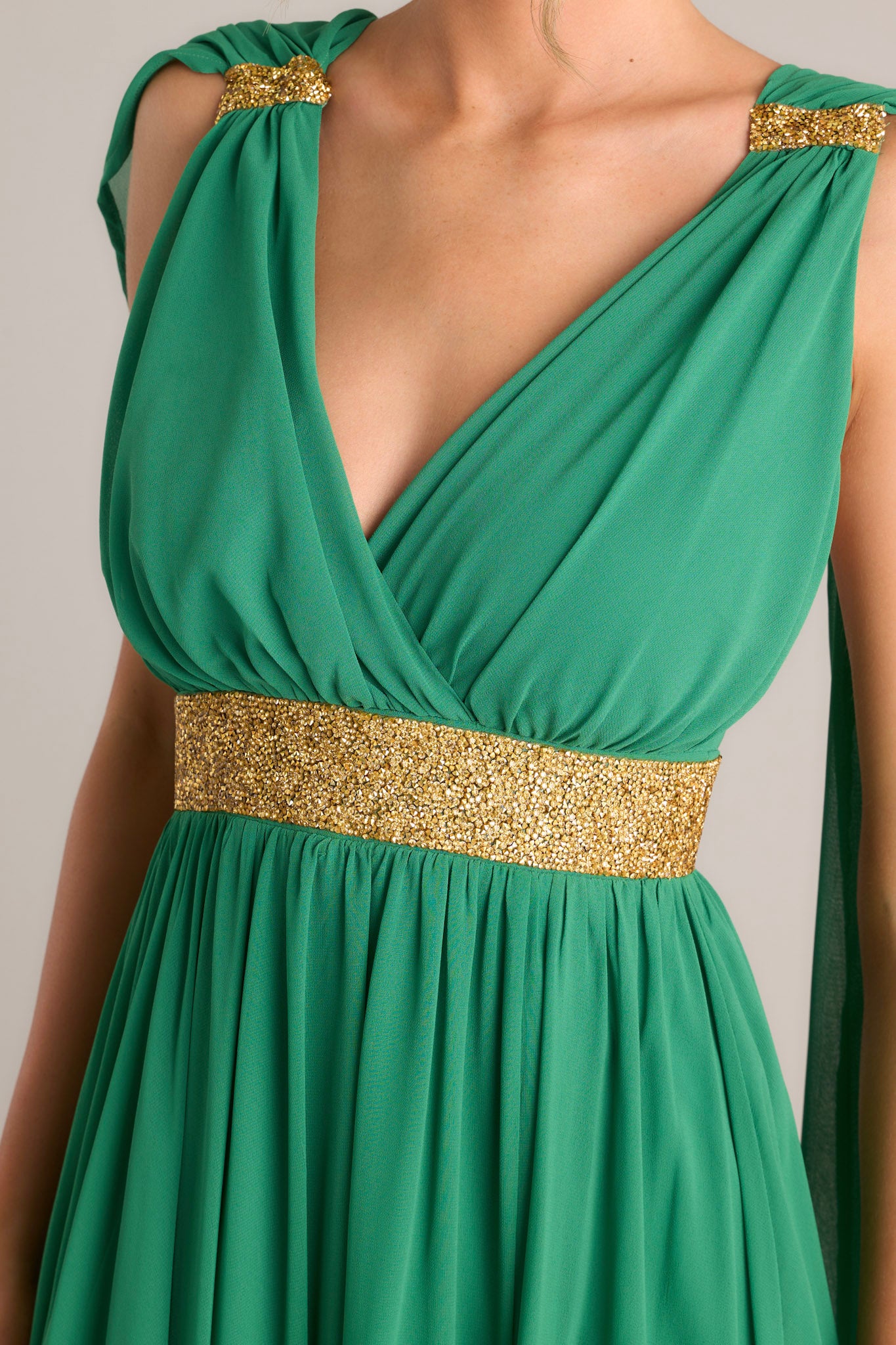 Close-up of the green dress showing the v-neckline, rhinestone detailing, and fabric trailing from the shoulder.