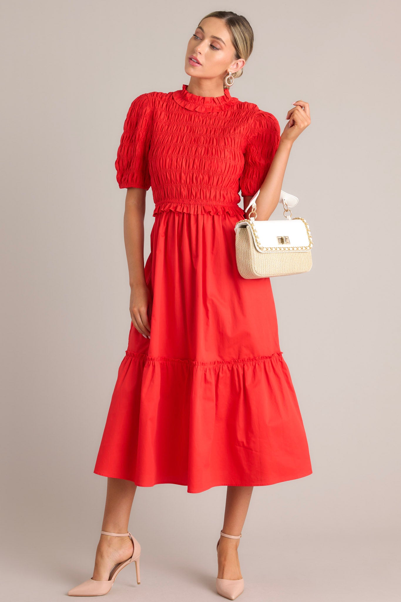 Angled full body view of this red midi dress that features high ruffled neckline, a keyhole with button closure, a fully smocked bodice, a tiered design, a fully smocked elastic cuffed half sleeves.