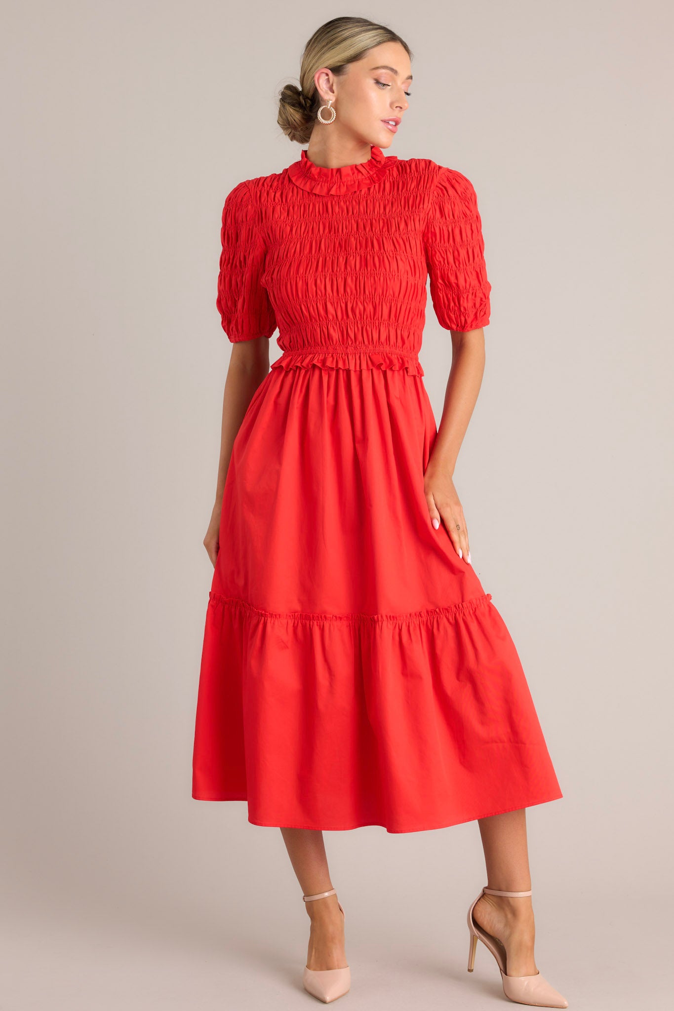 Front view of this red midi dress that features high ruffled neckline, a keyhole with button closure, a fully smocked bodice, a tiered design, a fully smocked elastic cuffed half sleeves.