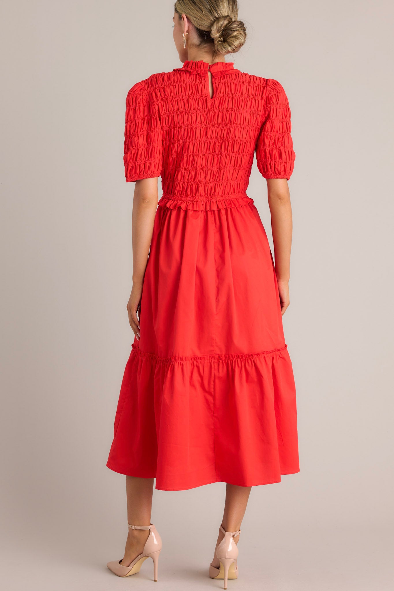 Back view of this red midi dress that features high ruffled neckline, a keyhole with button closure, a fully smocked bodice, a tiered design, a fully smocked elastic cuffed half sleeves.
