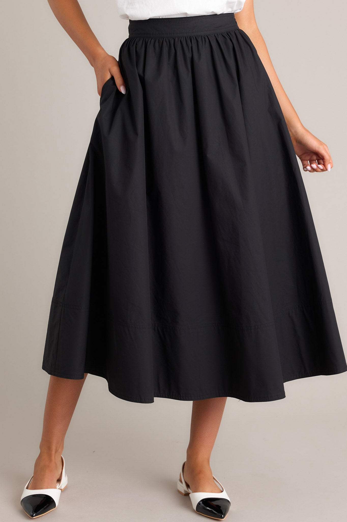 Front view of a black 100% cotton midi skirt featuring a high waisted design, functional hip pockets, and a thick hemline.