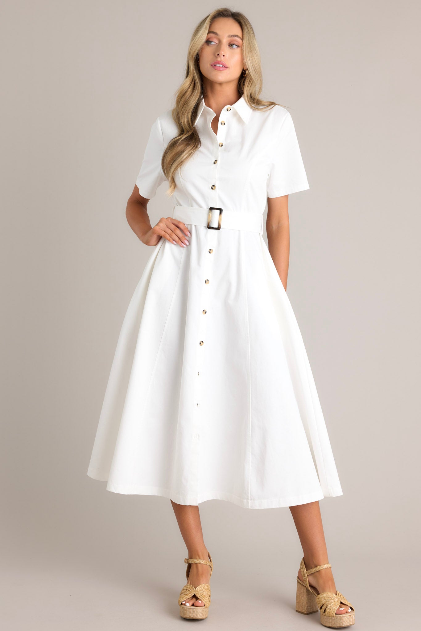 Front view of this white midi dress that features a collared neckline, a full button front, a functional pull-through belt, functional hip pockets, and short sleeves.