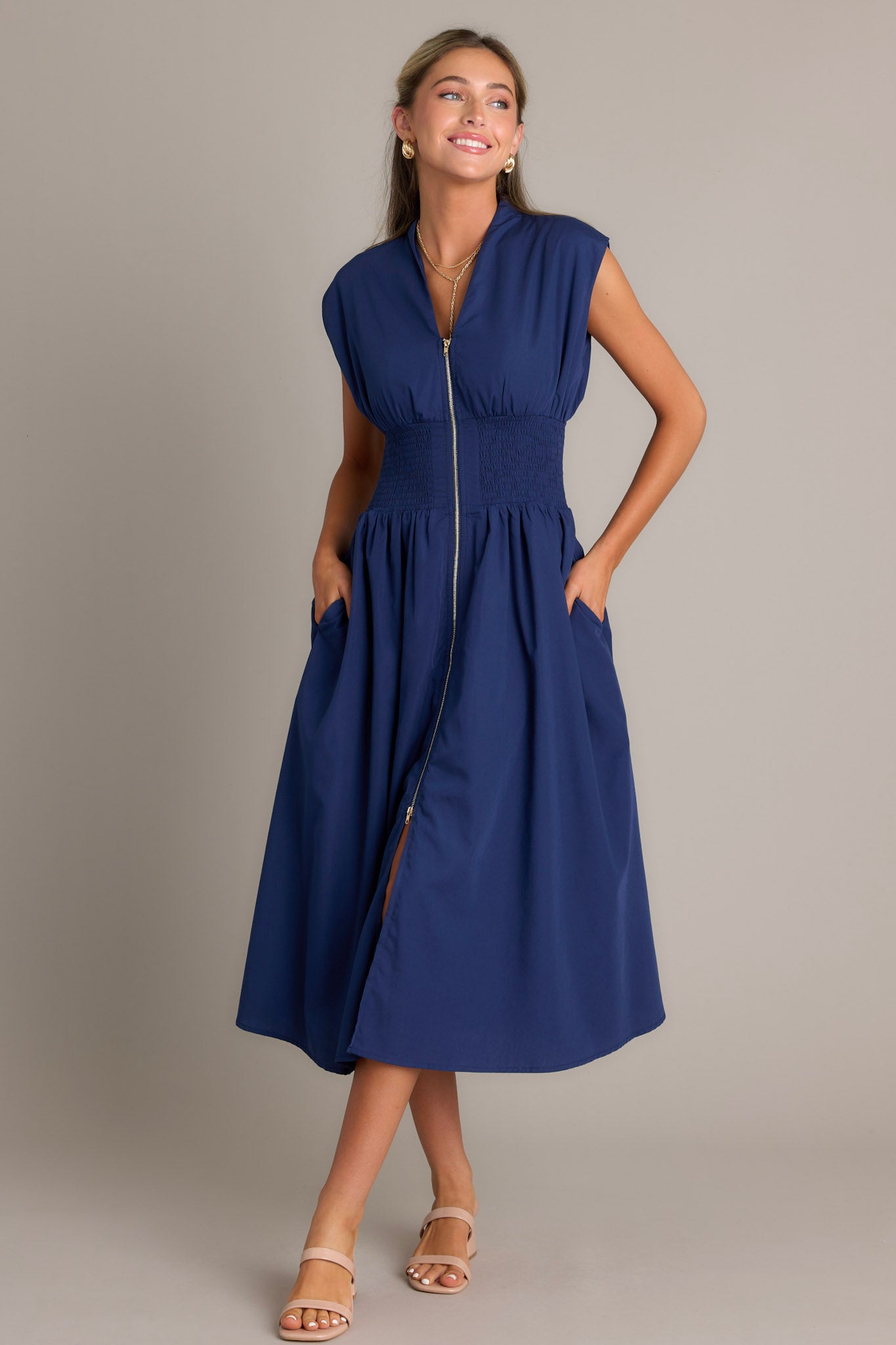 view of a navy blue dress featuring a V-neckline, cap sleeves, a zippered front, and a cinched waist with shirred detailing, highlighting its stylish and elegant design.