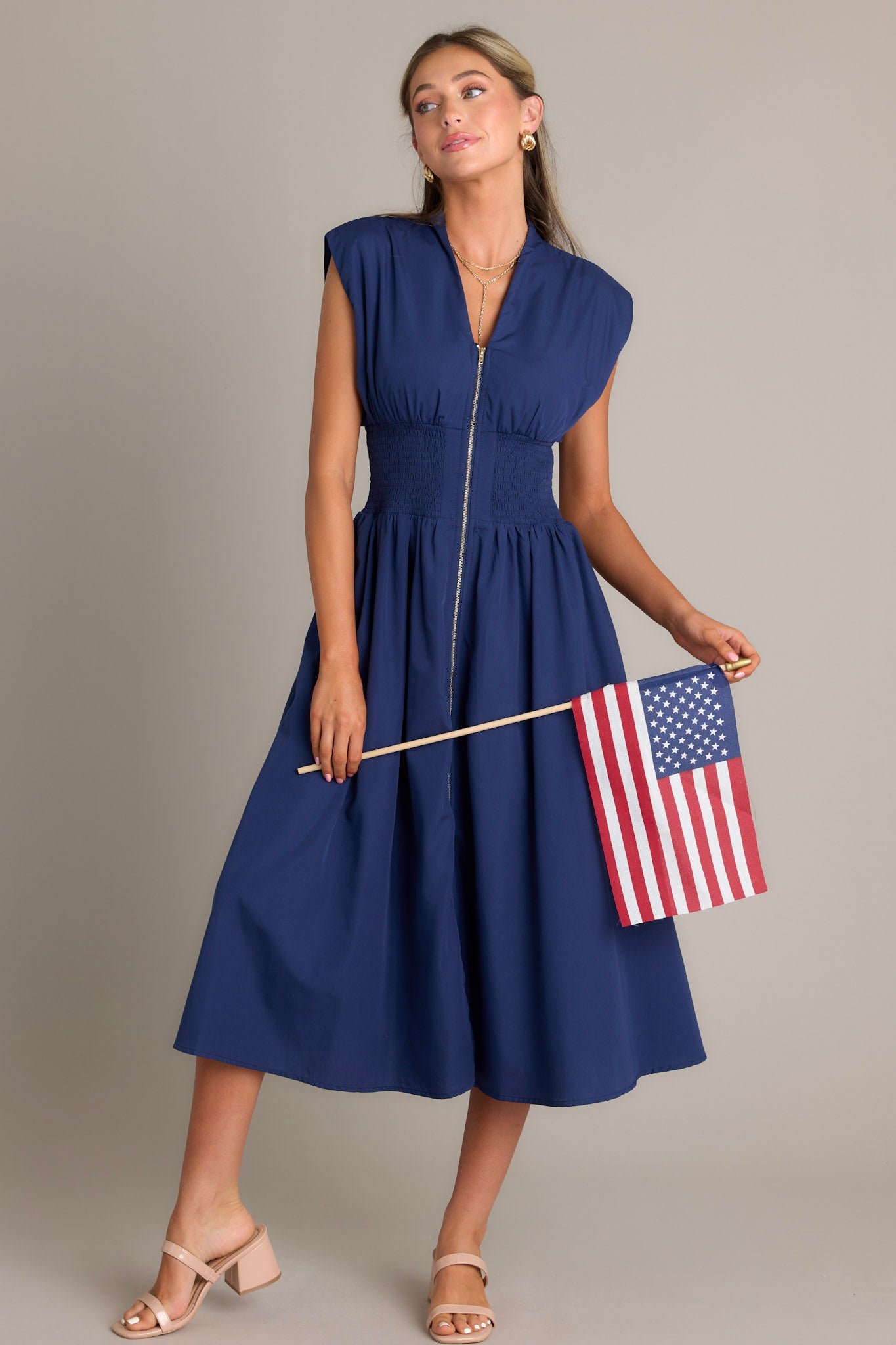 Full body view of a navy blue dress with a V-neckline, cap sleeves, a zippered front, and a cinched waist, showcasing a stylish and elegant design.
