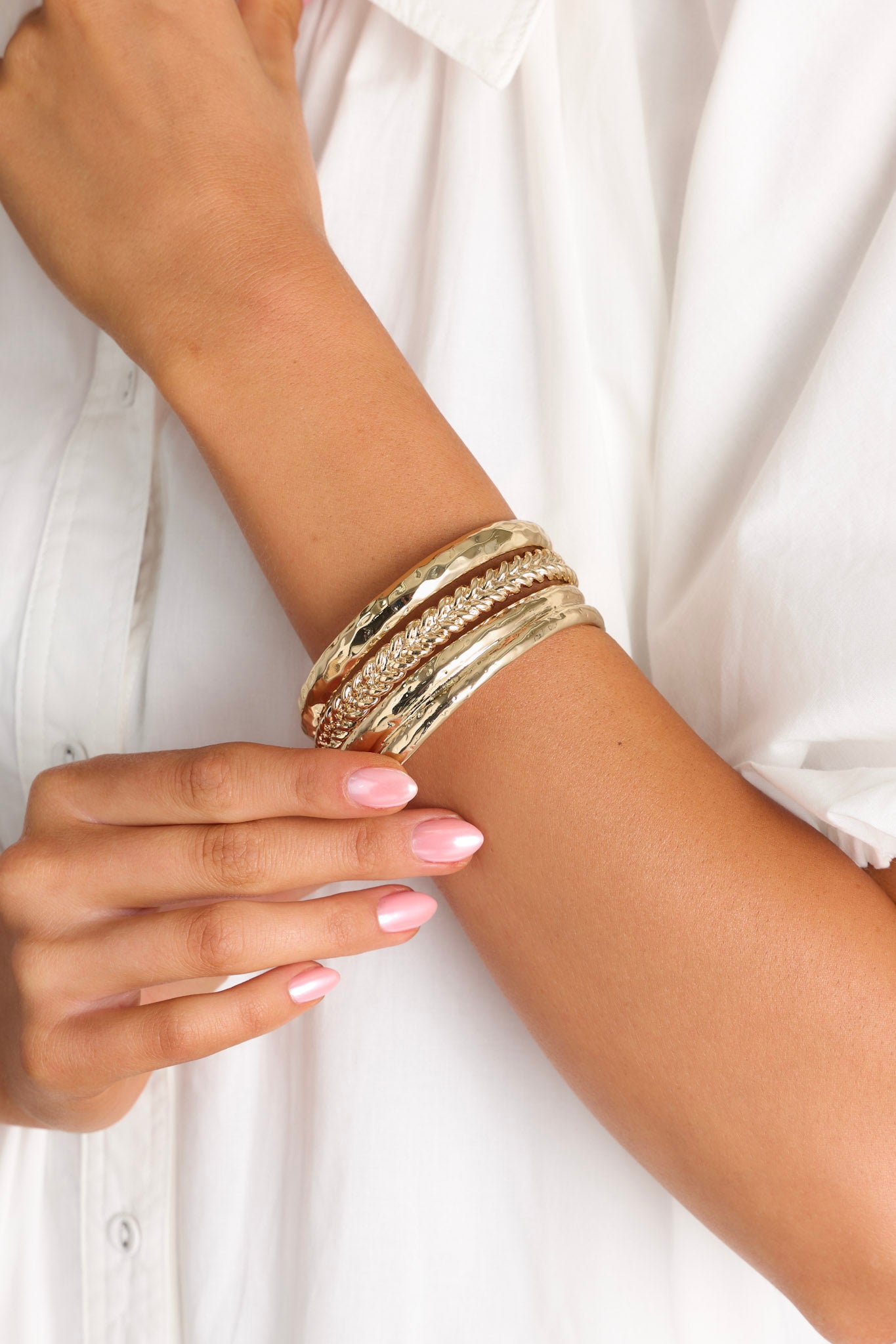 These gold bangles feature gold hardware, two textured bangles, and one bangle with a braided design.