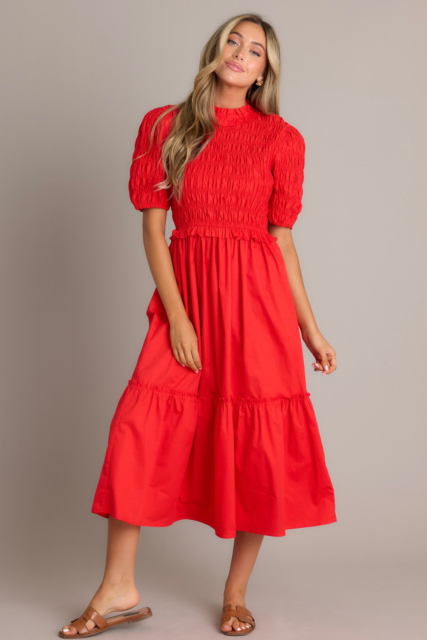 Full body view of this red midi dress that features high ruffled neckline, a keyhole with button closure, a fully smocked bodice, a tiered design, a fully smocked elastic cuffed half sleeves.