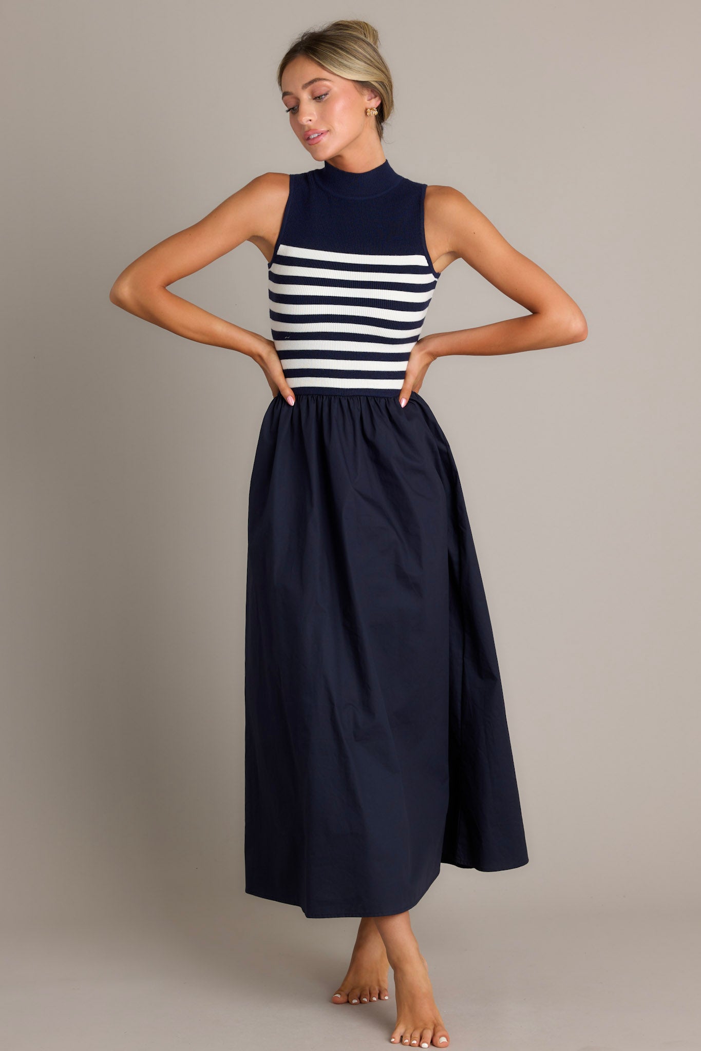 Full body view of this navy stripe maxi dress that features a high neckline, a striped sweater bodice, and a flowy skirt.