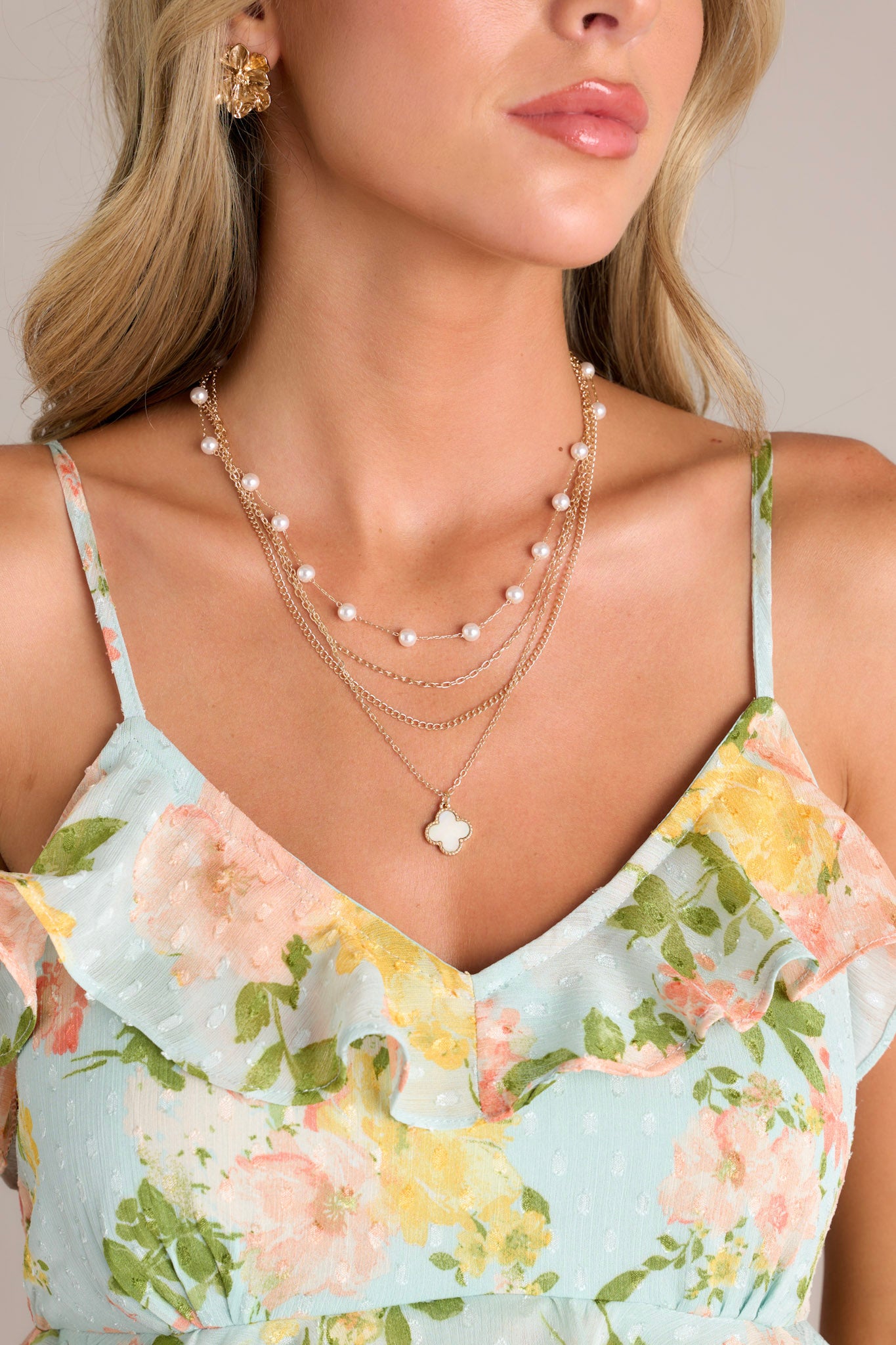 This gold necklace features gold hardware, a faux pearl chain, a chain with a iridescent clover charm, two thin gold chains, and a lobster claw clasp.