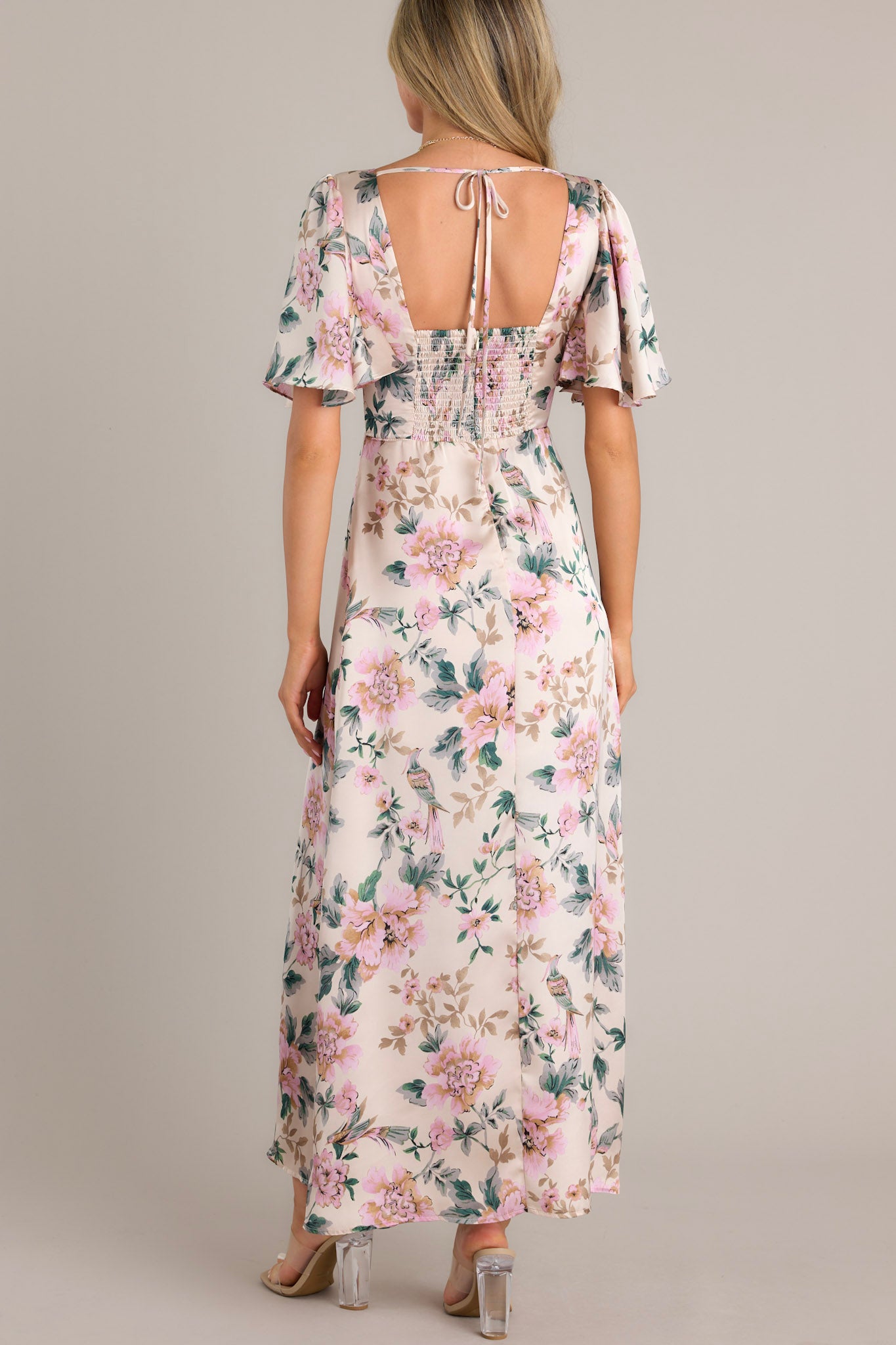 Back view of this ivory floral maxi dress featuring a deep V-neckline, flutter sleeves, fitted waist, and A-line skirt with a floral print.