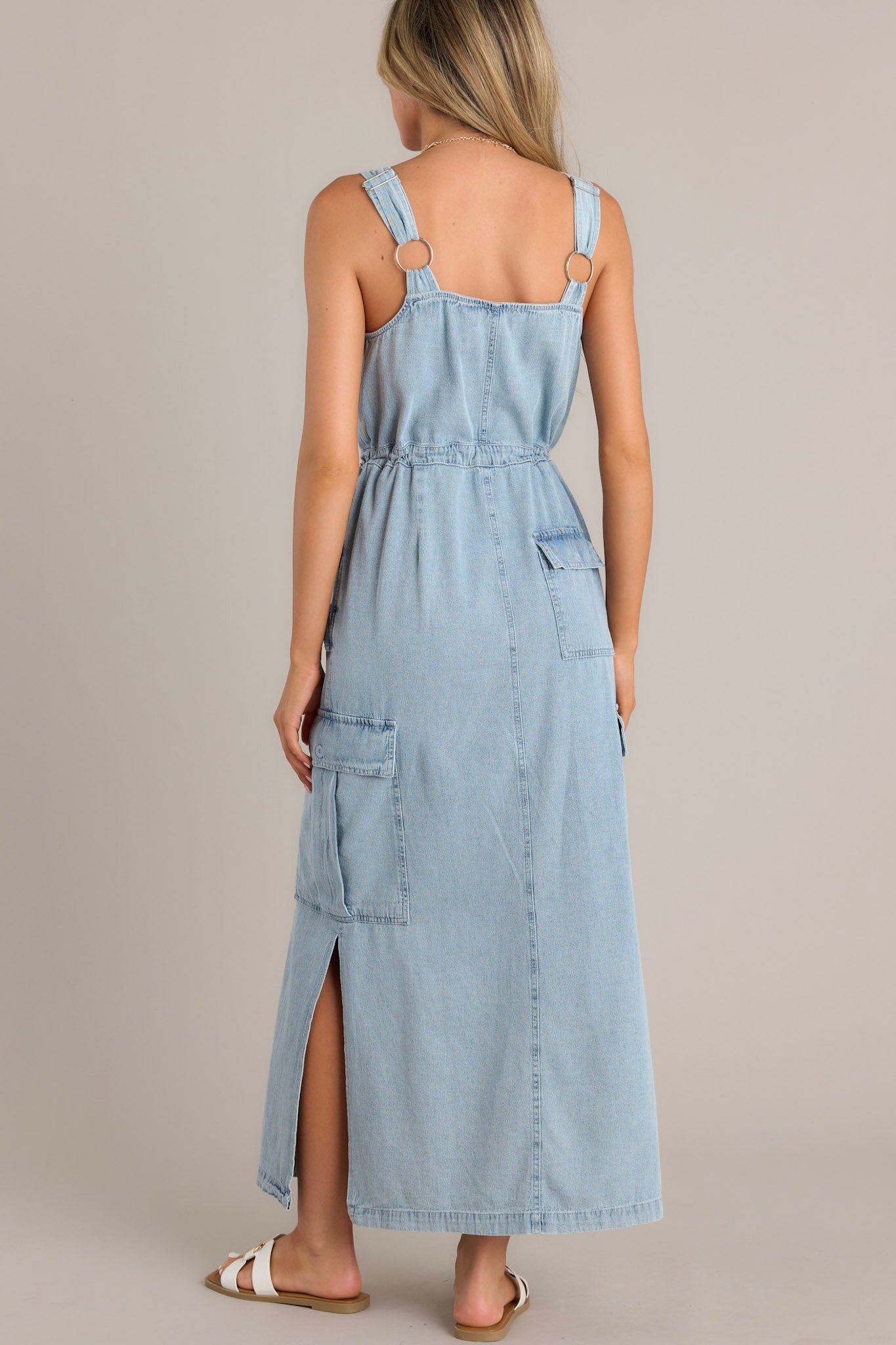 Back view of a chambray maxi dress featuring thick adjustable straps, functional button back pockets, and a self-tie drawstring waist.