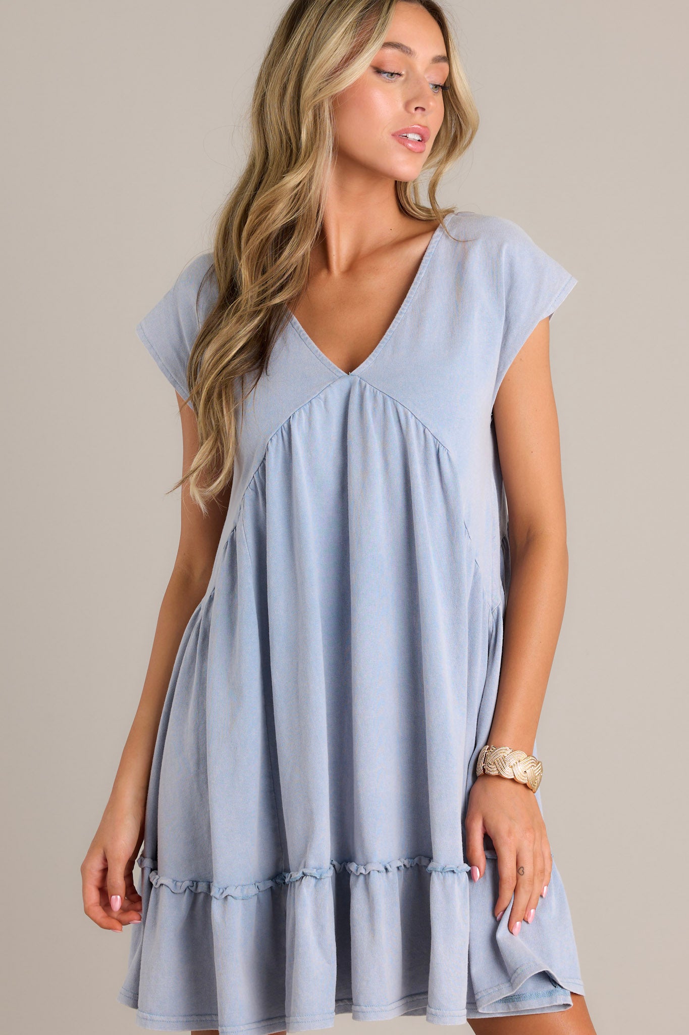 This blue mini dress features a v-neckline, ruching below the bust line, and short cap sleeves.