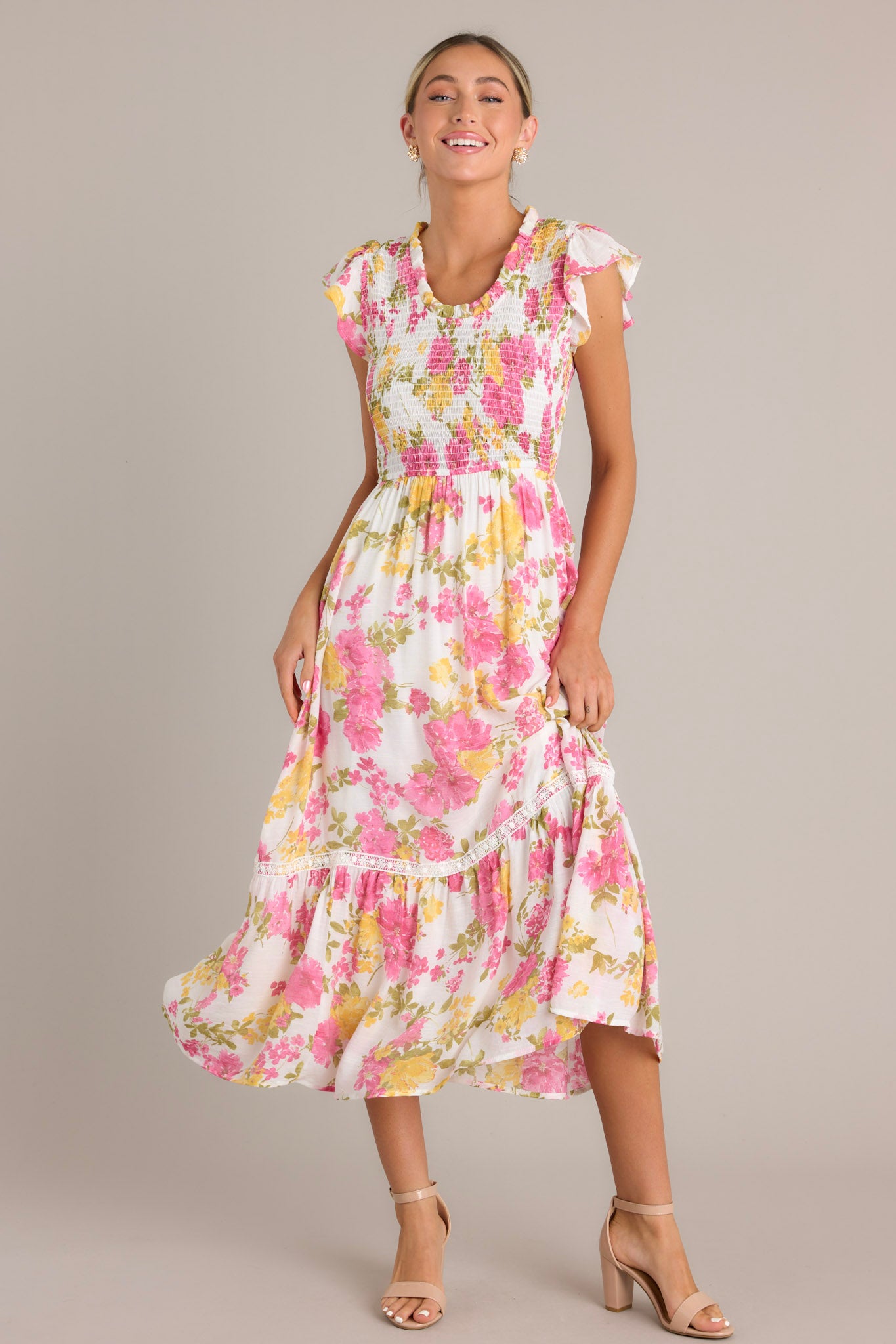 A white and pink floral midi dress with a ruffled scoop neckline and a fully smocked bodice, complete with short flutter sleeves.