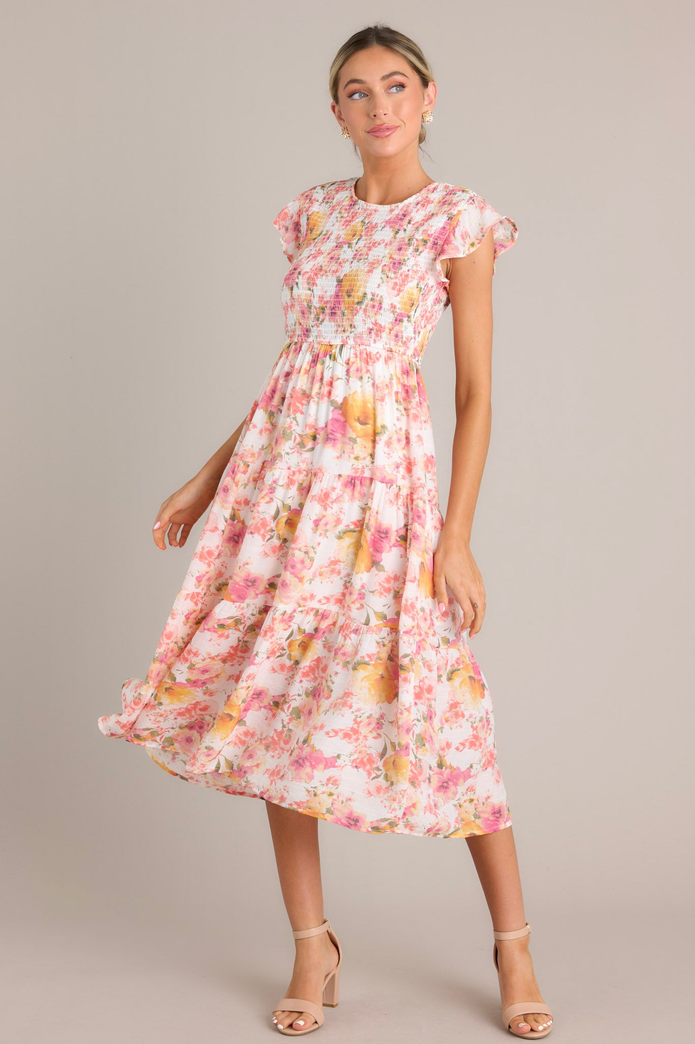 Floral midi dress in pink with a high neckline, flutter sleeves, smocked bodice, tiered structure, and floral print.
