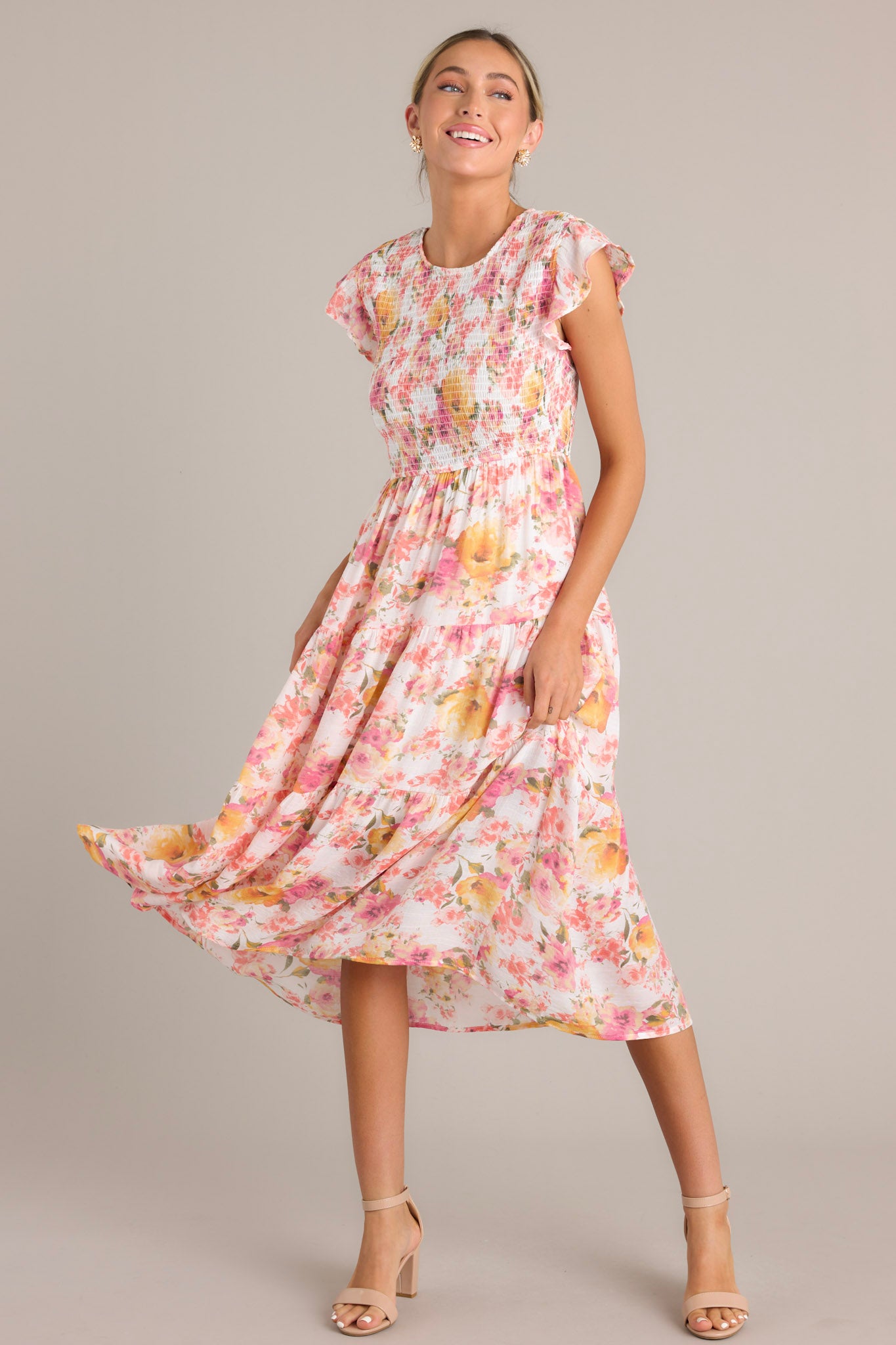 Pink floral midi dress with a high neckline, flutter sleeves, fully smocked bodice, tiered design, and vibrant floral pattern.